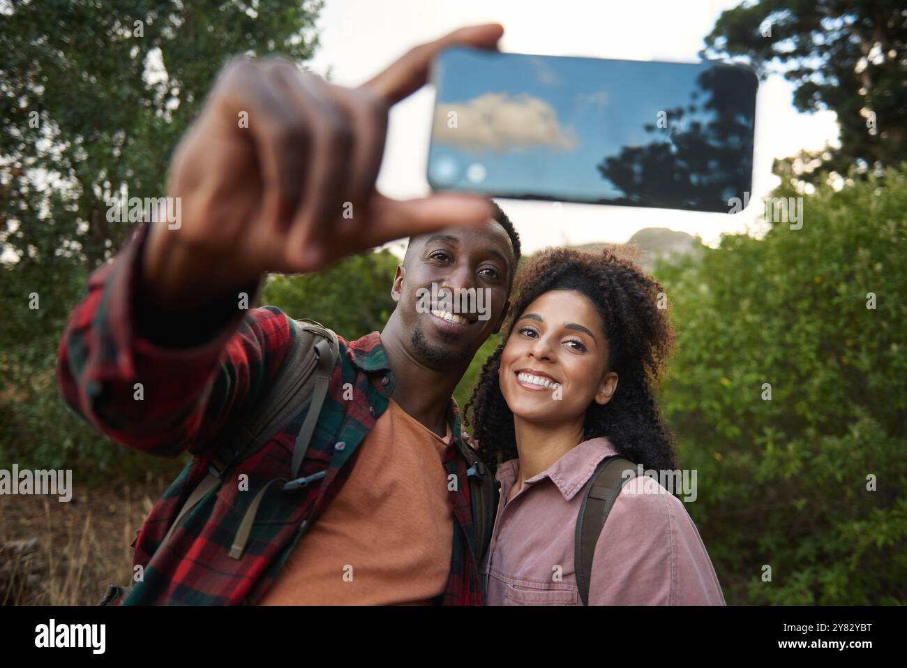 Portrait d'un jeune couple multiethnique souriant et prenant un selfie smartphone ensemble pendant une randonnée dans quelques collines accidentées en été Banque D'Images