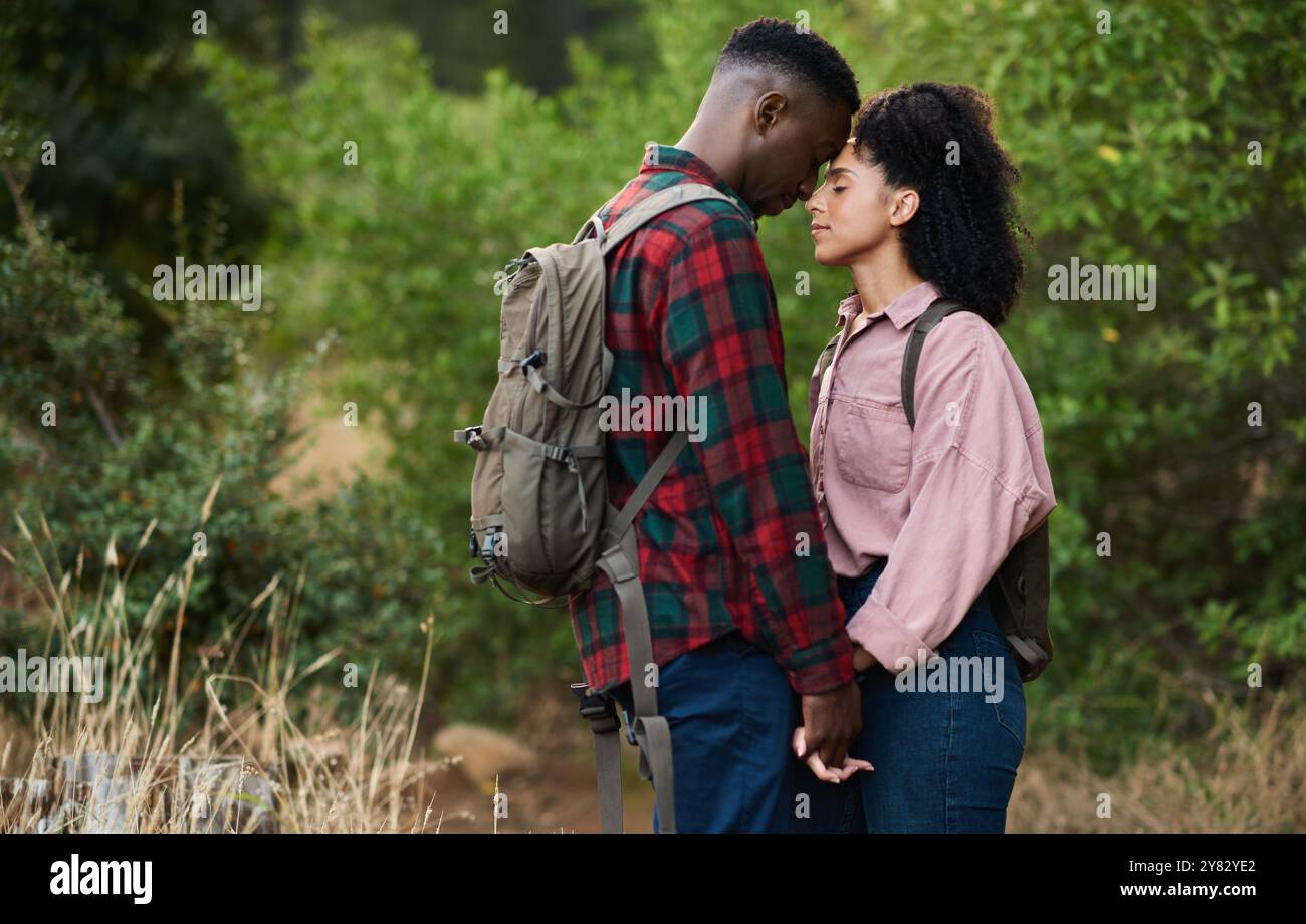 Aimant jeune couple multiethnique debout face à face avec les yeux fermés sur un sentier lors d'une pause de hikine dans certaines collines en été Banque D'Images
