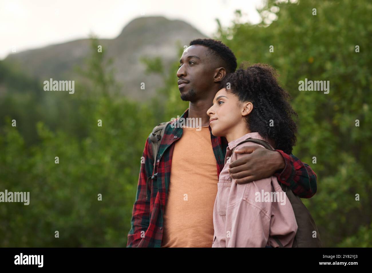 Jeune couple multiethnique profitant de la vue panoramique alors que dehors pour une randonnée ensemble dans quelques collines accidentées en été Banque D'Images
