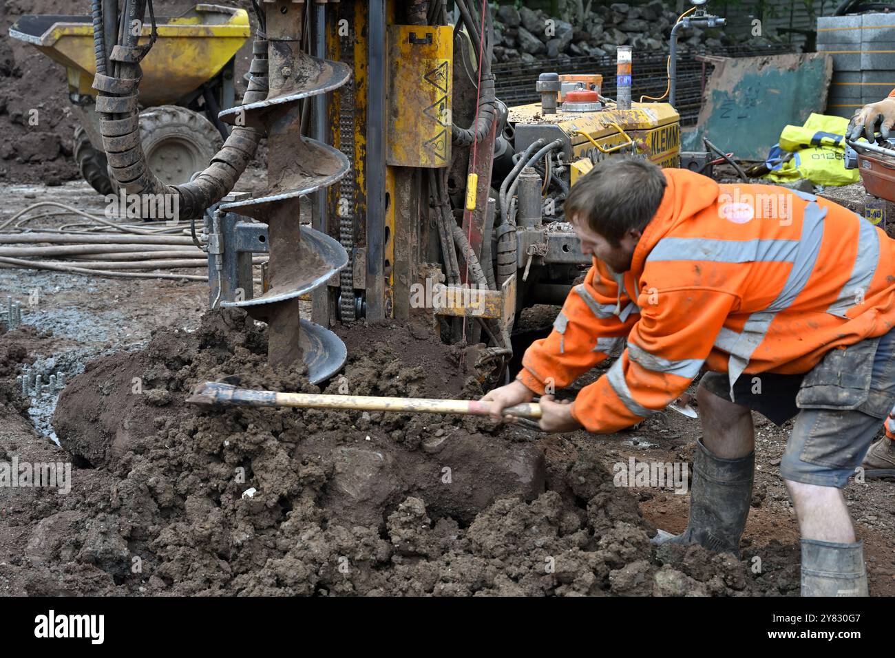 Homme déblayant manuellement les déblais de la machine de forage de pieux de tarière perçant le trou dans le sol argileux sur le chantier de construction domestique Banque D'Images