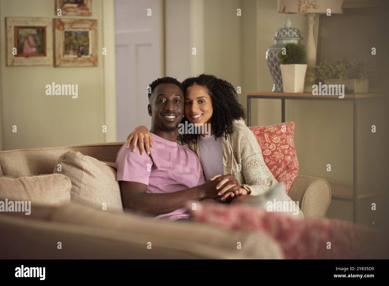 Portrait d'un jeune couple multiracial affectueux souriant tout en étant assis ensemble sur leur canapé de salon à la maison Banque D'Images