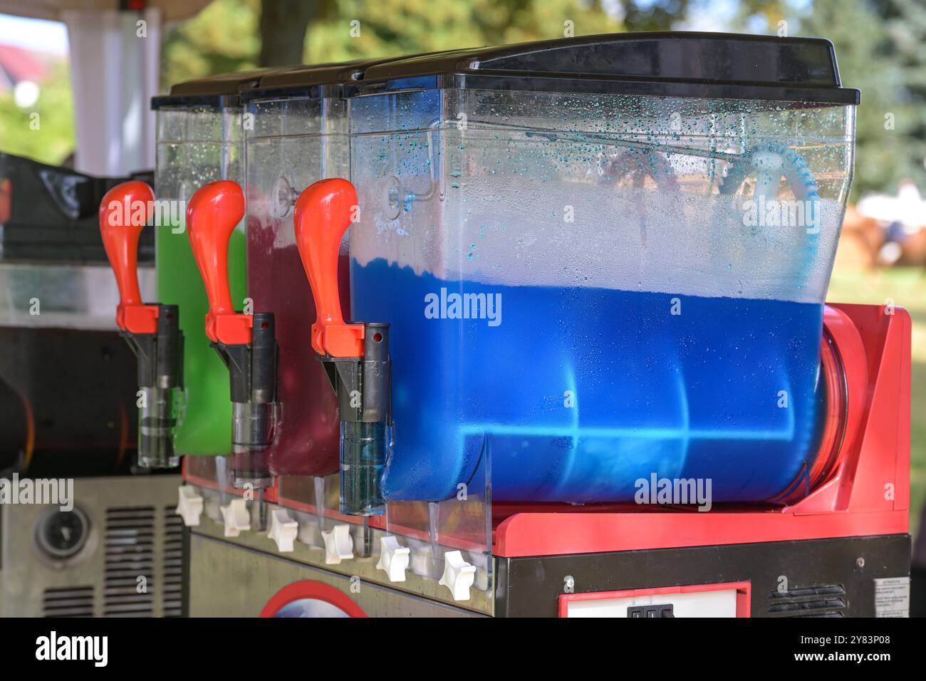 Machine à slush faisant des boissons glacées colorées avec différentes saveurs, boissons rafraîchissantes avec de la glace en bleu, rouge et vert à un marché funfair, sélectionné Banque D'Images