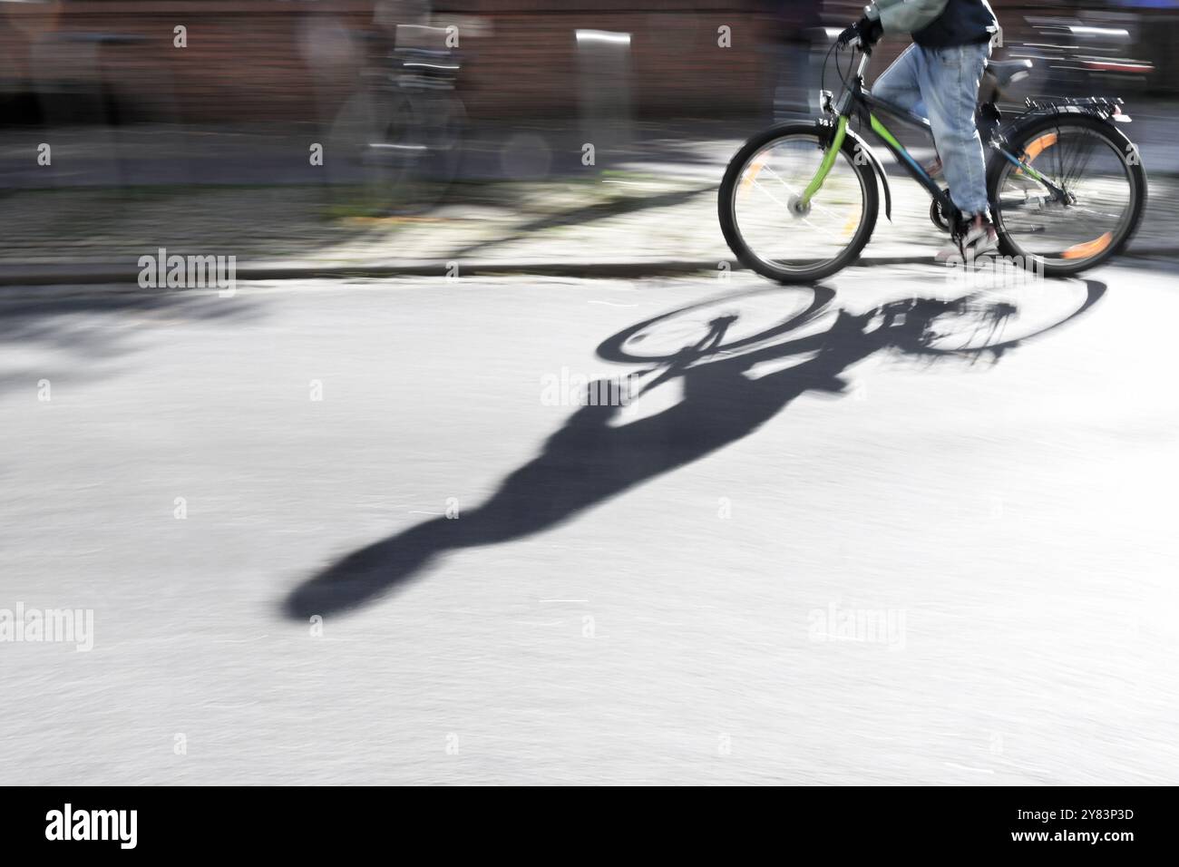 Partie d'un jeune homme à vélo dans la rue dans la ville, projetant une longue ombre sur l'asphalte, panoramique de la photographie avec flou de mouvement, espace de copie Banque D'Images