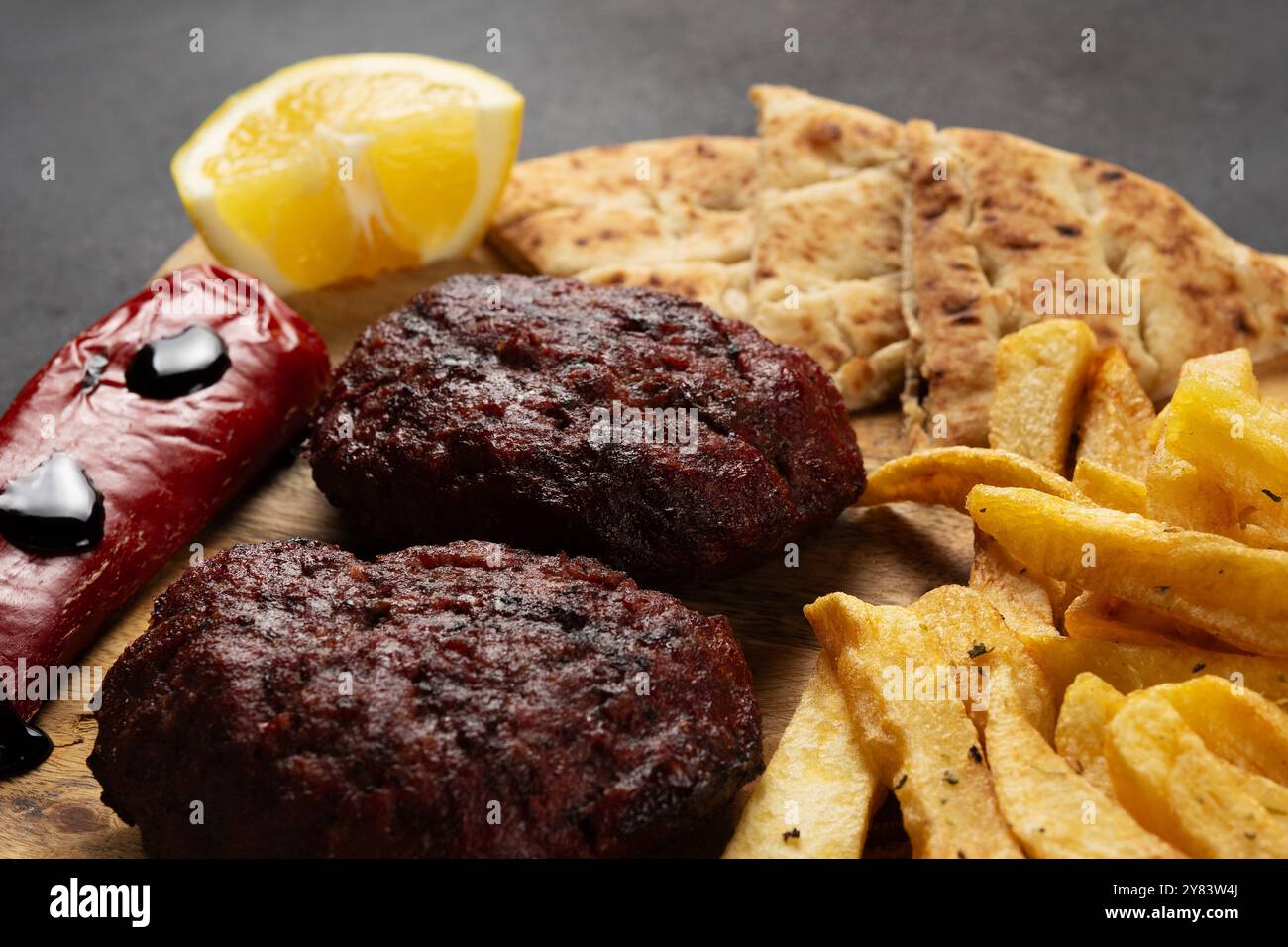 Vue rapprochée de patty de boeuf à base de viande hachée avec pommes de terre frites, poivre, pita et trempette de yaourt sur planche de bois. Banque D'Images