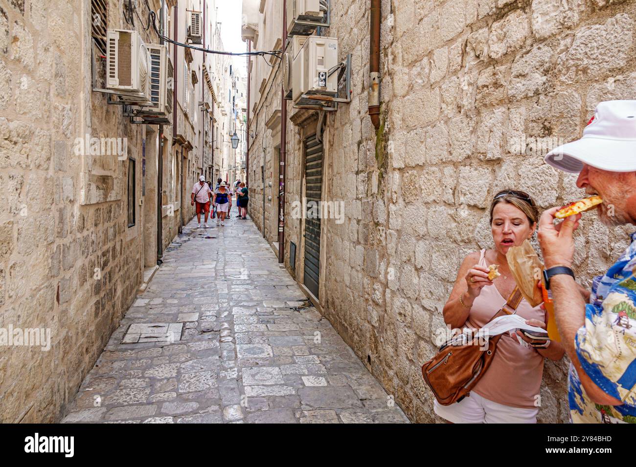 Dubrovnik Croatie, vieille ville, ruelle piétonne étroite pavée de calcaire, couple de femmes d'homme de visiteurs, debout manger grignoter pizza pâtisserie, bal croate Banque D'Images