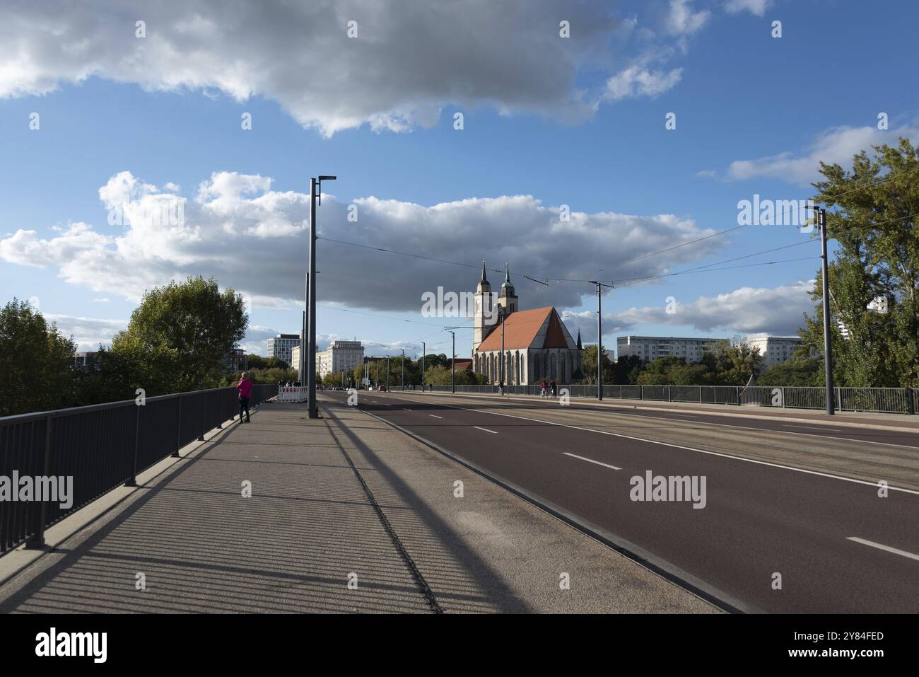 Un pont mène à l'église Saint-Jean avec son toit rouge et deux tours, entouré de bâtiments de la ville moderne sous un ciel partiellement nuageux, Magdebourg, Saxe- Banque D'Images