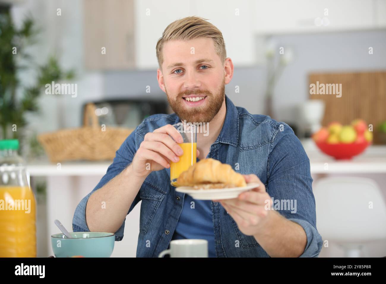 homme à la table du petit déjeuner offrant un croissant Banque D'Images