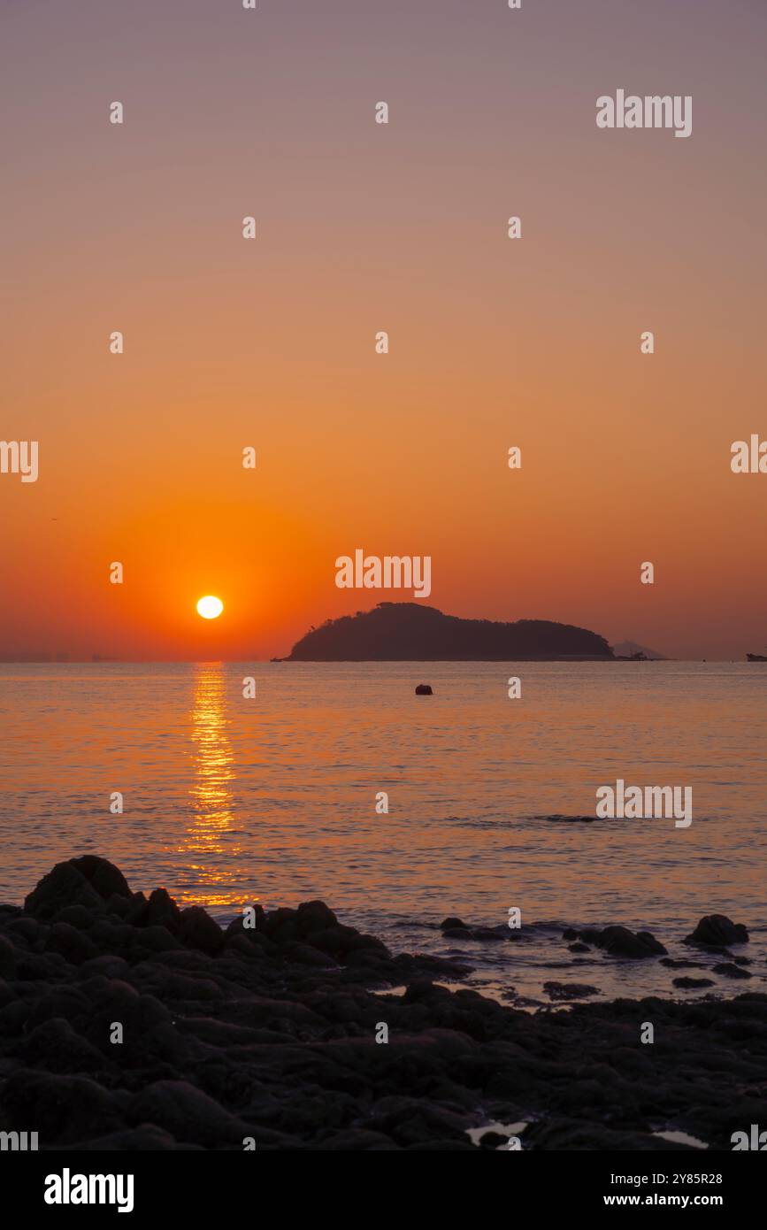 Un lever de soleil serein sur Jamjindo Island, Incheon. Le soleil se reflète sur la mer calme, jetant un chemin doré, avec des rochers au premier plan. Banque D'Images