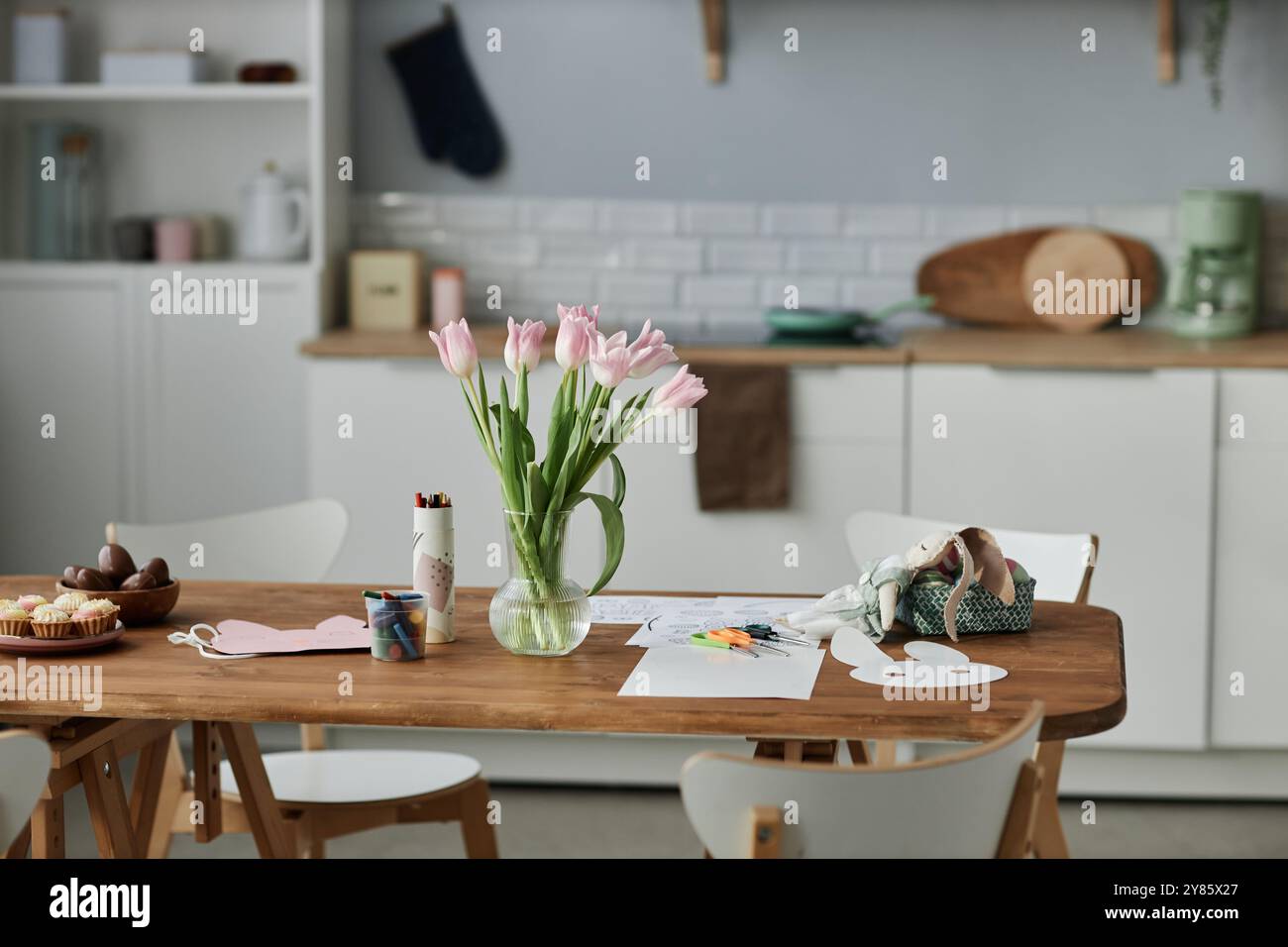 Tulipes fraîches dans un vase sur une table en bois entourée de diverses fournitures d'artisanat, y compris des coeurs en papier, des marqueurs et des ciseaux dans un cadre de cuisine confortable Banque D'Images
