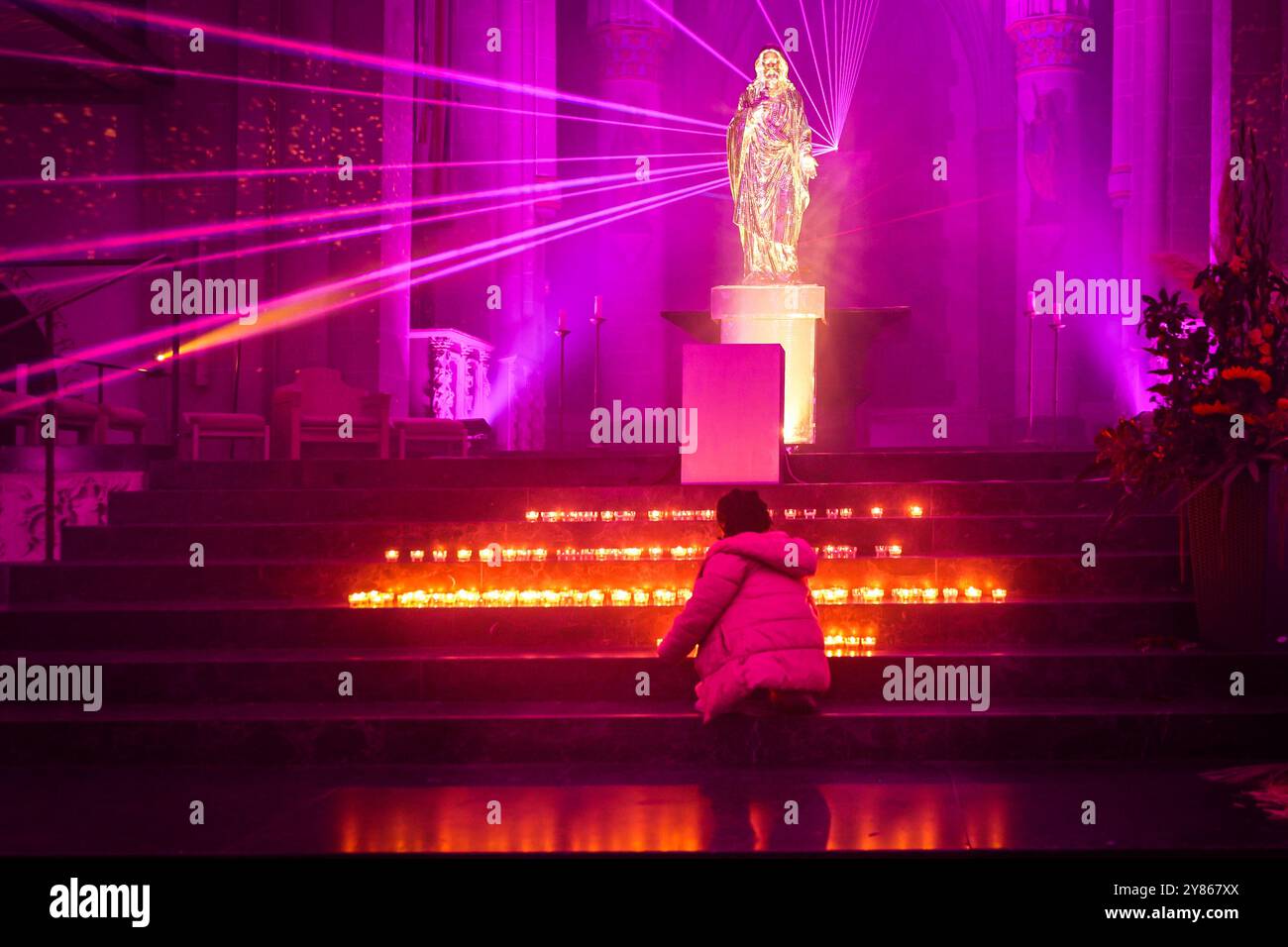 Essen, NRW, Allemagne, 02 octobre 2024. Une fille pose une bougie. Les visiteurs de la cathédrale d'Essen interagissent avec le vibrant et inspirant 'Salvator Mundi | Licht & Segen 1' du collectif d'art SilentMOD, une installation lumineuse et laser multisensuelle avec des carreaux en miroir flottant à l'intérieur de la cathédrale, et des faisceaux laser derrière une statue en miroir de Jésus. Soirée d'ouverture du festival annuel des lumières d'Essen, qui présente 16 grandes installations lumineuses spectaculaires le long d'un parcours de randonnée à travers la ville. Le festival gratuit est gratuit et se déroulera tous les jours du 2 au 13 octobre 2024. Banque D'Images