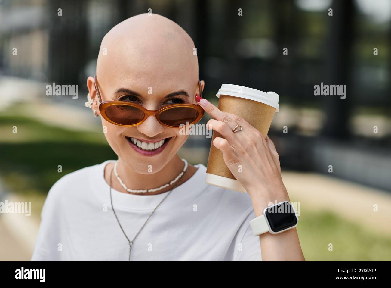 Une jeune femme chauve habillée élégamment sourit alors qu'elle tient une tasse de café et profite de sa journée. Banque D'Images