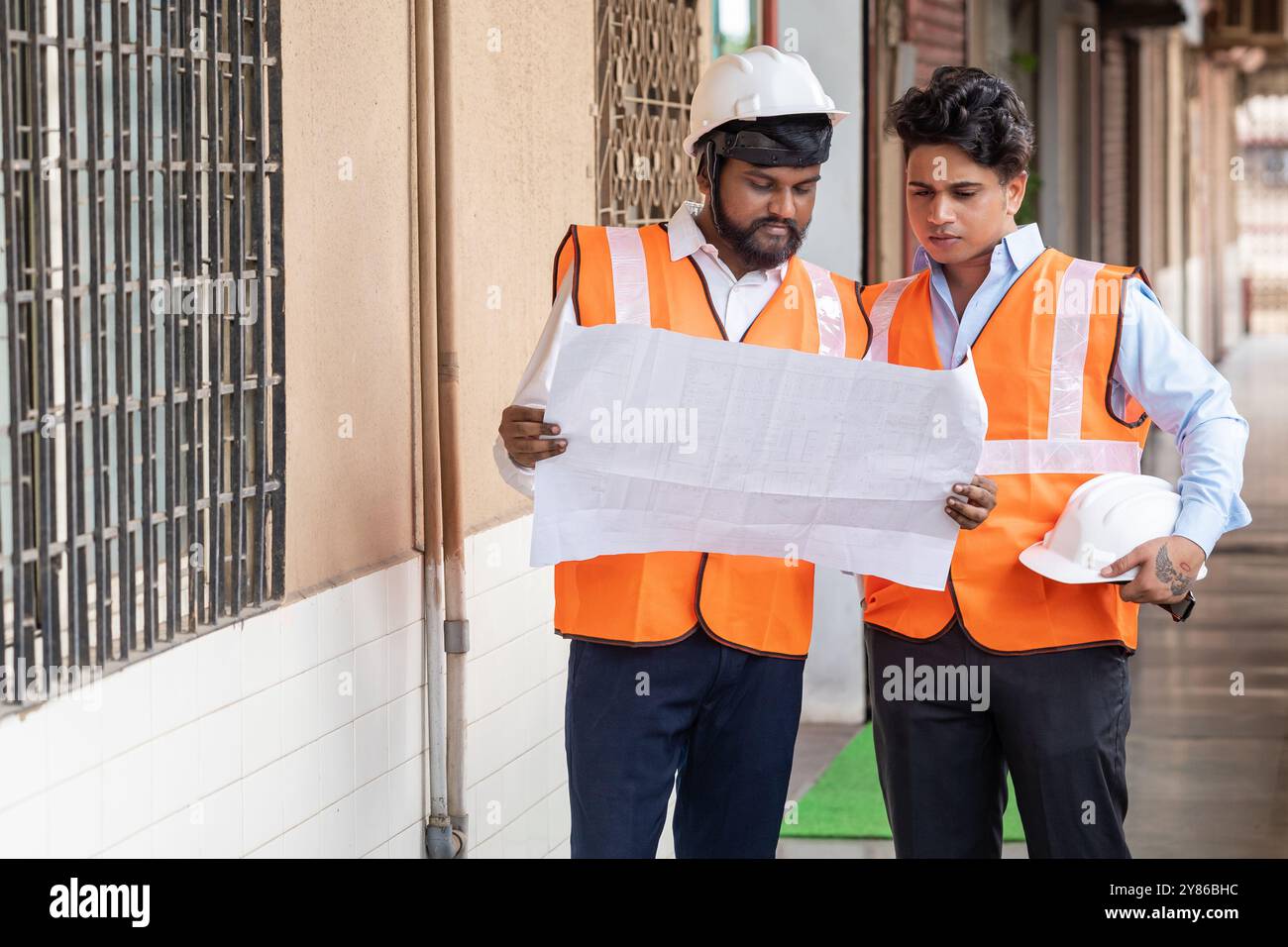 Travail d'équipe ciblé où deux ingénieurs de projet et architectes concentrés sur un chantier de construction, examinant avec diligence un plan ou un plan d'étage portant tous les deux Banque D'Images