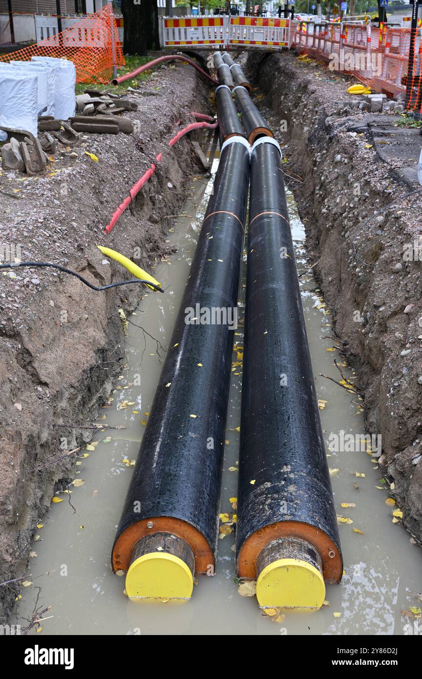 L'image montre un chantier de construction axé sur l'installation de grandes conduites souterraines. Deux grands tuyaux isolés sont visibles dans une tranchée remplie de W. Banque D'Images