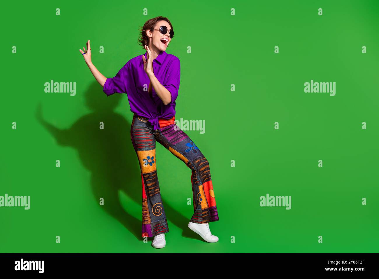 Portrait photo de la jeune dame positive avec les cheveux bob portant des lunettes de soleil élégantes pantalons baggy dansant aime les boîtes de nuit isolées sur fond de couleur verte Banque D'Images