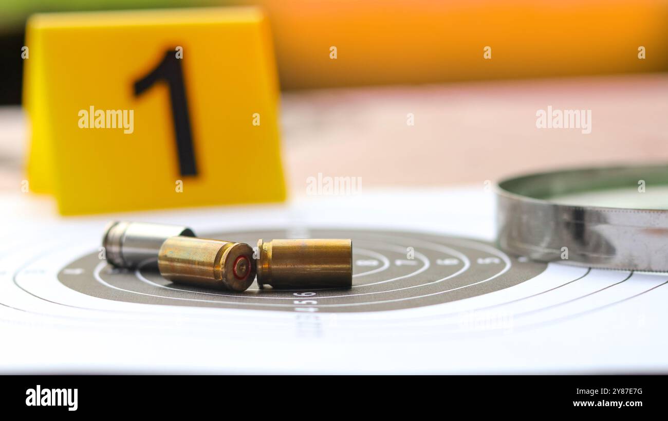 Enveloppes de balles vides sur un fond de cible de tir, avec le numéro noir flou 1 sur l'étiquette jaune et une loupe placée à proximité, mélangeant les thèmes Banque D'Images