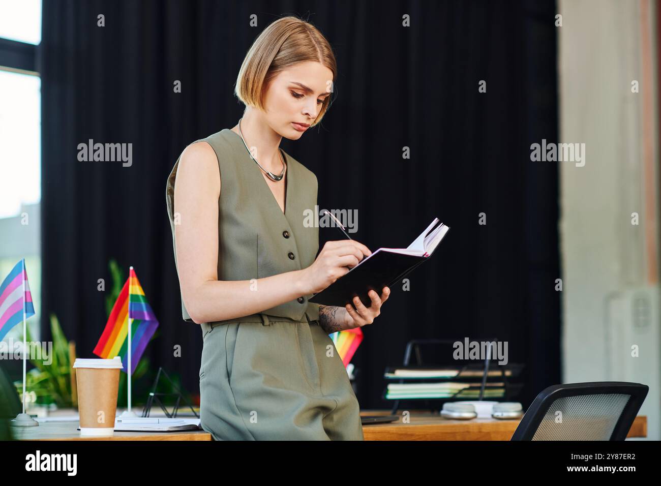 Une femme écrit des notes tout en étant entourée de symboles de fierté dans un environnement de bureau coloré. Banque D'Images