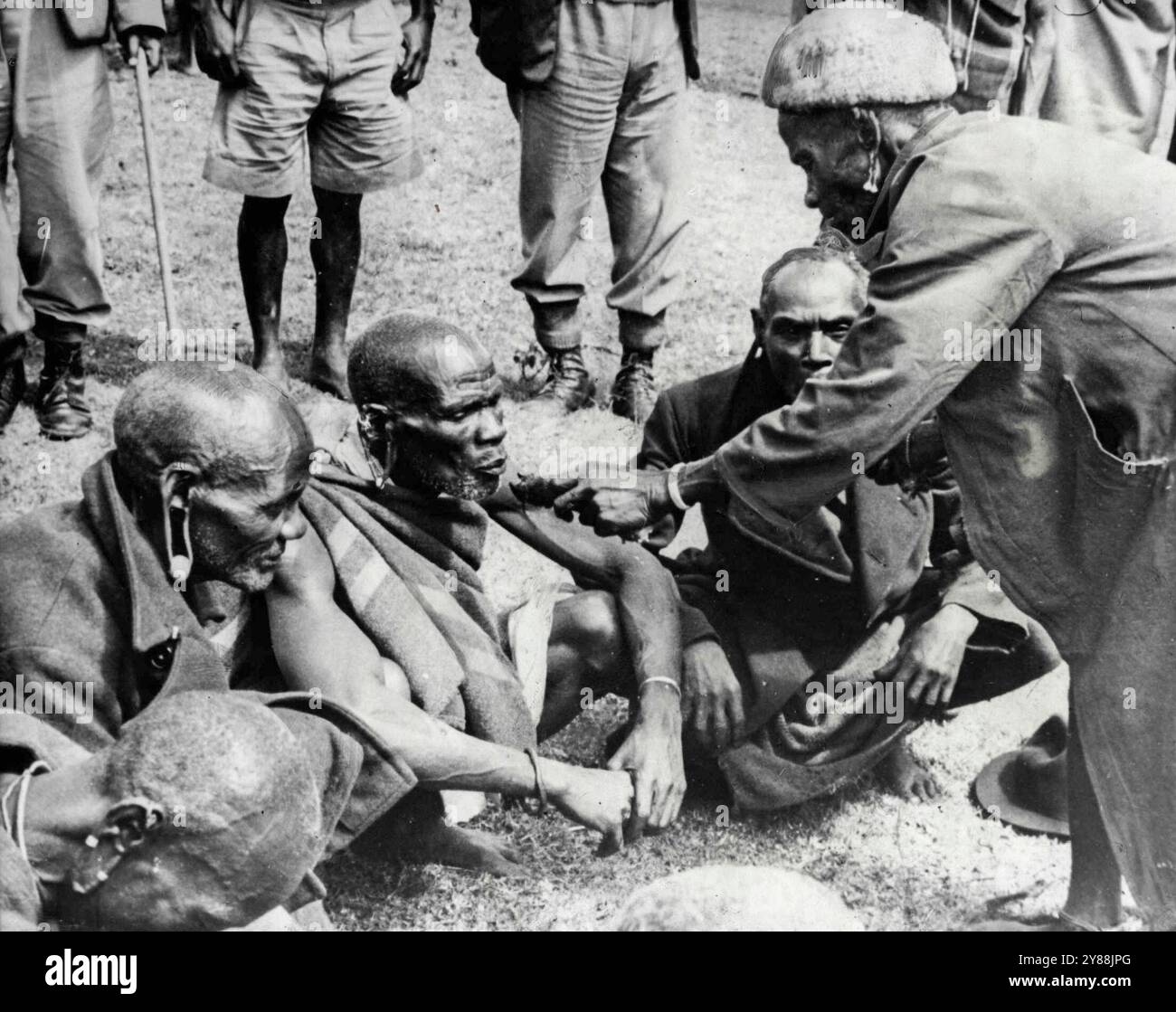 Mau,Mau nettoyage CeremonyCe est la première photo prise d'une cérémonie de nettoyage Mau,Mau dans le district de Kiambu au Kenya. Sur la droite, en pelage de peau de mouton, le Mundo Mu Gu' (Un sorcier qui pratique pour le bien et non pour le mal), se prépare à absoudre les membres de la tribu Kikuyu qui ont déjà prêté serment Mau,Mau. Devant le sorcier se trouve une dépression dans le sol bordée de feuilles de banane, contenant le sang et le contenu de l'estomac d'une chèvre abattue à cet effet. Le sabot de la chèvre, enveloppé dans des feuilles, est un trempé dans le sang et s'applique à la langue des initiés, qui répand alors le Mau M. Banque D'Images