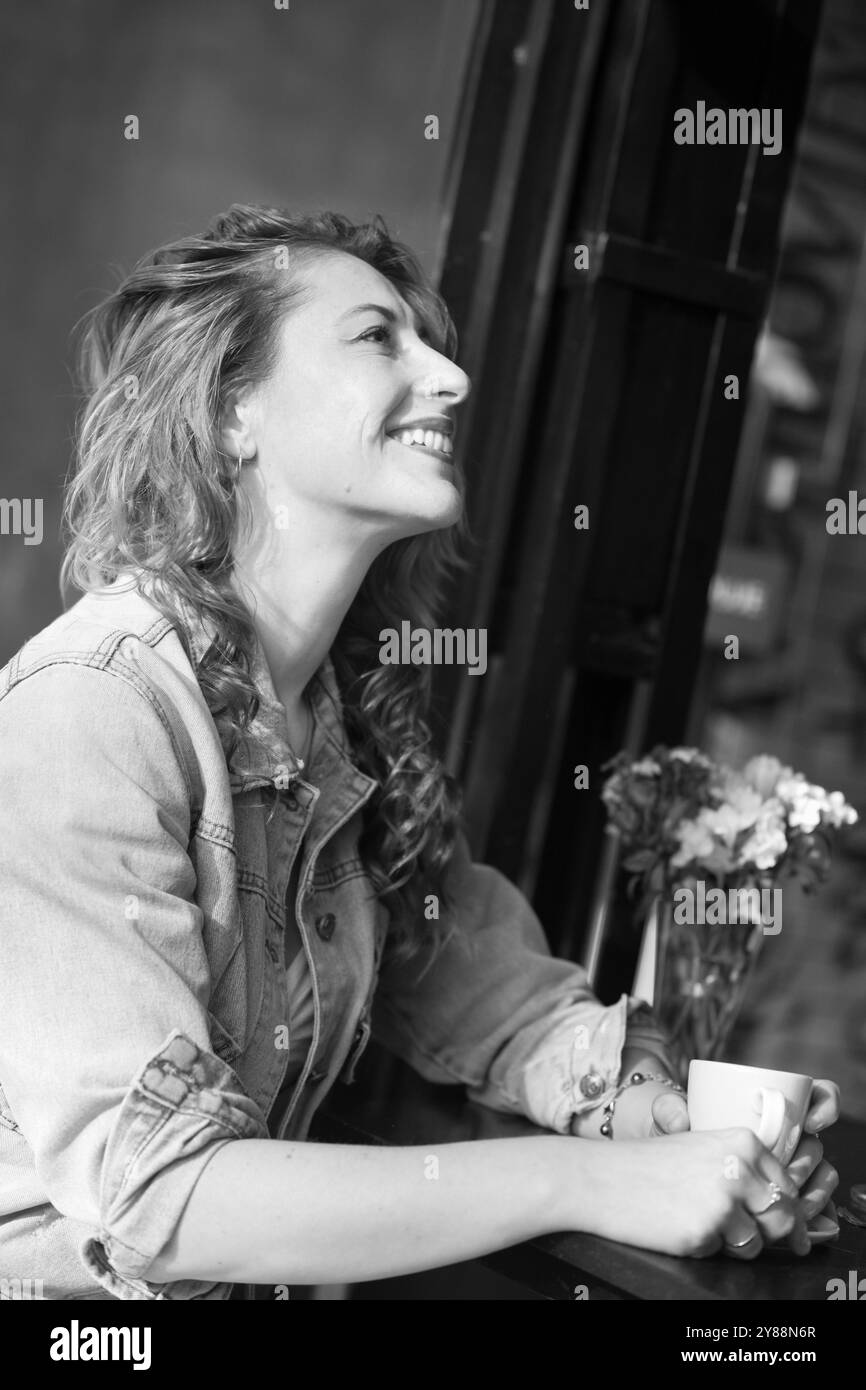 femme adulte moyenne joyeuse avec des cheveux de gingembre buvant du café dans le café de trottoir le matin ensoleillé Banque D'Images