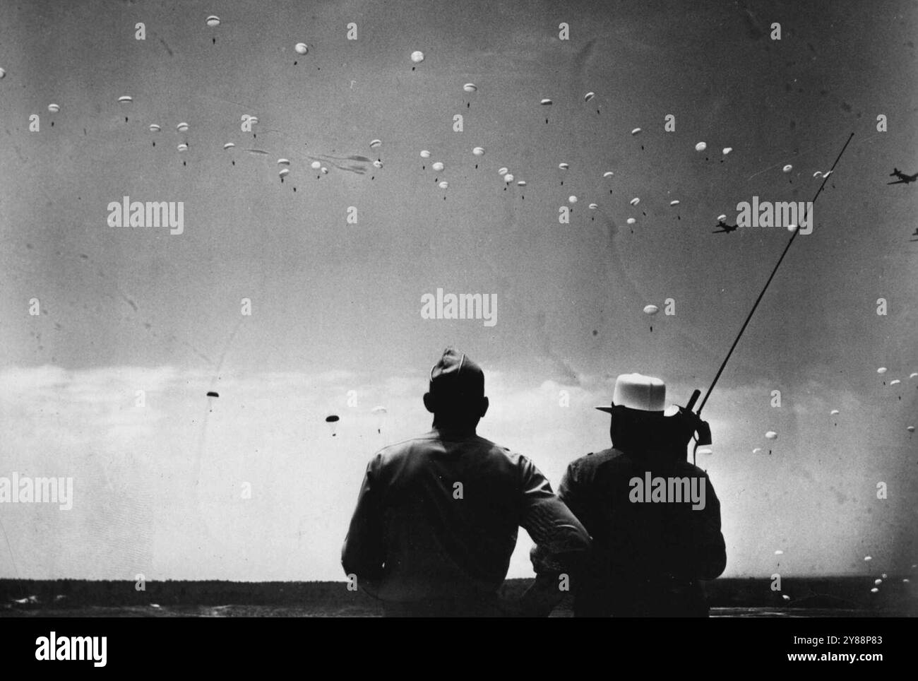 Churchill voit Sky Show des parachutistes américains - le premier ministre britannique Winston Churchill, lors de sa récente visite aux États-Unis, a assisté à cette exposition de sauts massifs en parachute dans un centre d'entraînement de l'armée américaine où des milliers de jeunes américains sont en train d'être entraînés dans le War­fare moderne, M.R. Churchill, debout à droite, a vu 600 soldats sauter et en même temps écouté les ordres des troupes par une radio, dont l'antenne peut être vue silhouettée contre le ciel. Avec le premier ministre se trouve le brigadier général William C. Lee, commandant de parachute. 03 septembre 1942. Banque D'Images