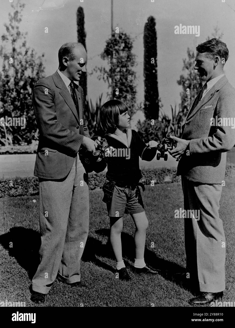 Vont-ils les utiliser Robert Coogan la jeune star de cinéma pense que W. Barwick (à gauche) et Alex Hillhouse les coureurs de fond trouveront ces patins utiles. On le voit faire la présentation tout en montrant les deux coureurs autour des studios Paramount à Hollywood. 9 août 1932. (Photo de London News Agency photos Ltd.). Banque D'Images