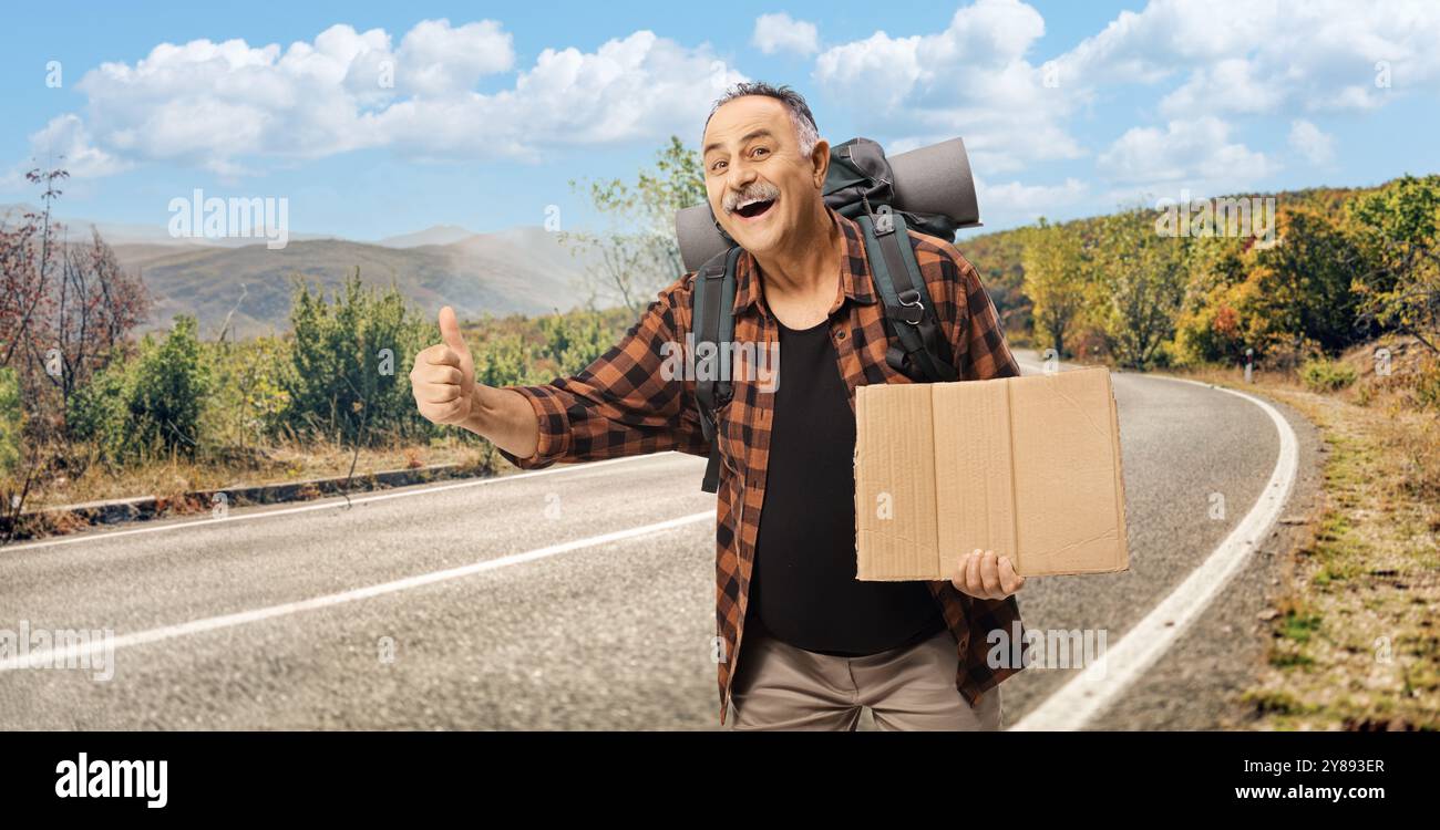 Homme mature souriant avec un sac à dos en auto-stop sur une route Banque D'Images