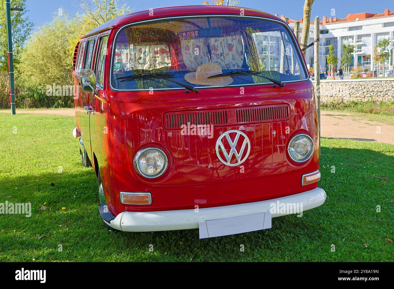 La fourgonnette volkswagen Kombi rouge est garée sur un terrain herbeux avec des bâtiments en arrière-plan Banque D'Images