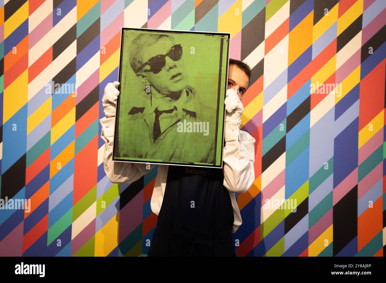 Un gestionnaire d'art tient l'Autoportrait d'Andy Warhol devant Gaillard 2 de Bridget Riley, lors d'un aperçu de la vente d'œuvres d'art Sotheby's de 200 millions de livres sterling, qui comprend des œuvres de Hockney, Warhol et Picasso. Date de la photo : vendredi 4 octobre 2024. Banque D'Images