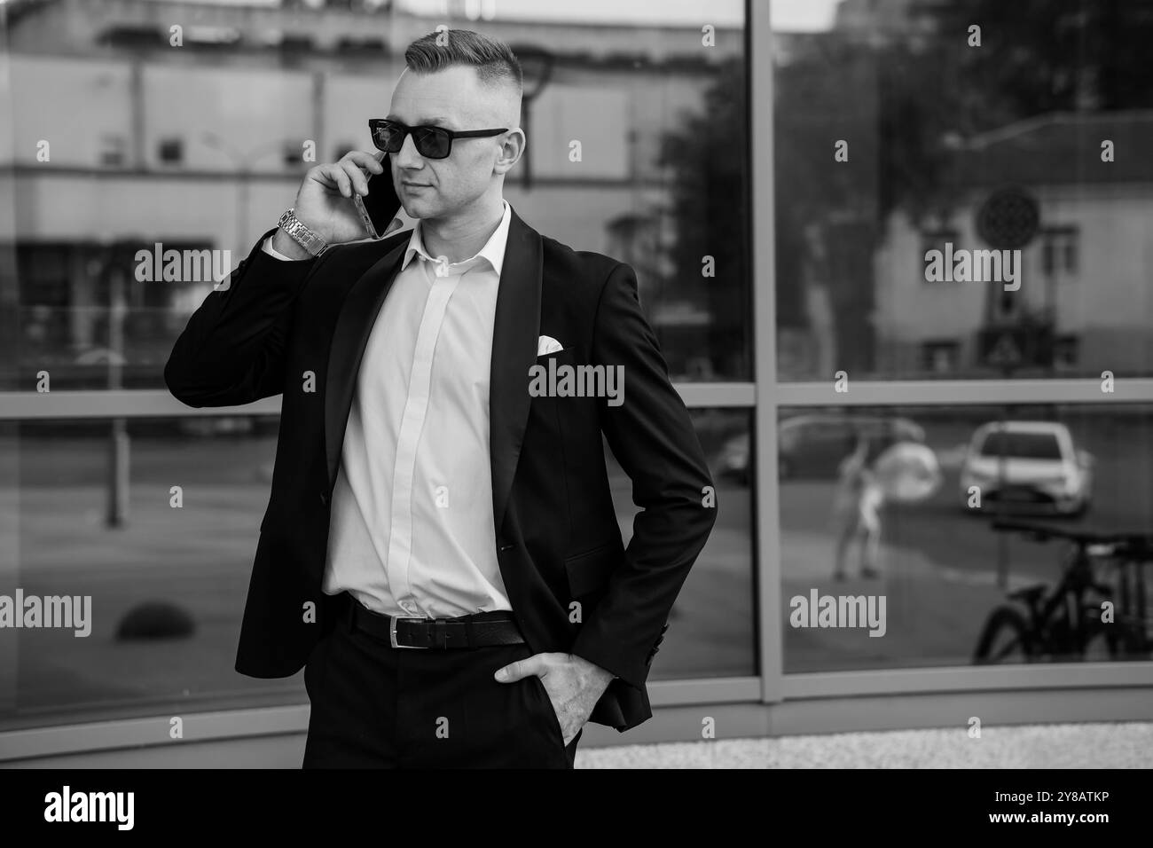Homme d'affaires confiant en costume élégant et lunettes de soleil engagés dans la conversation téléphonique. Banque D'Images