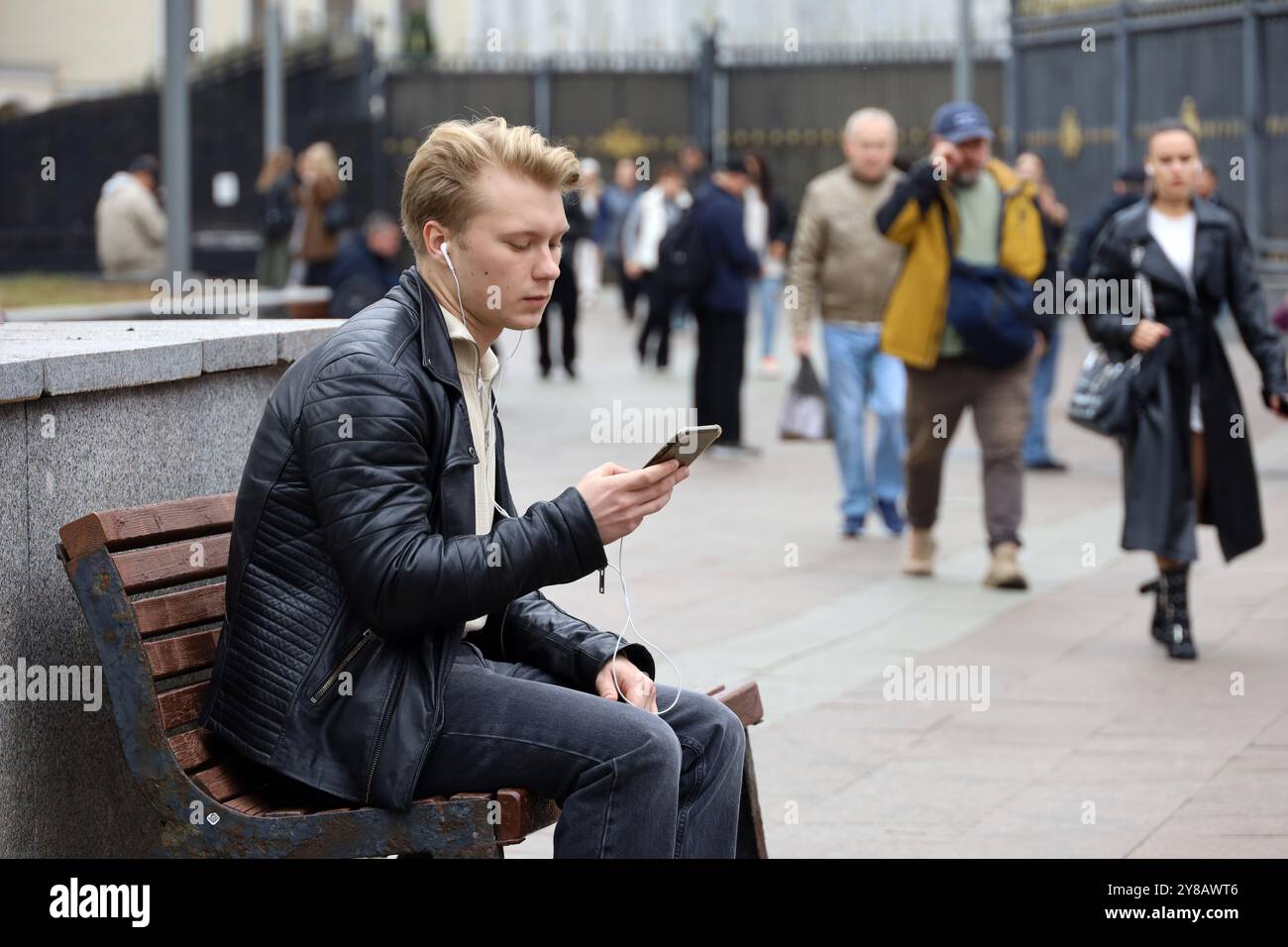 Gars dans des écouteurs assis avec smartphone sur le banc de rue en ville Banque D'Images