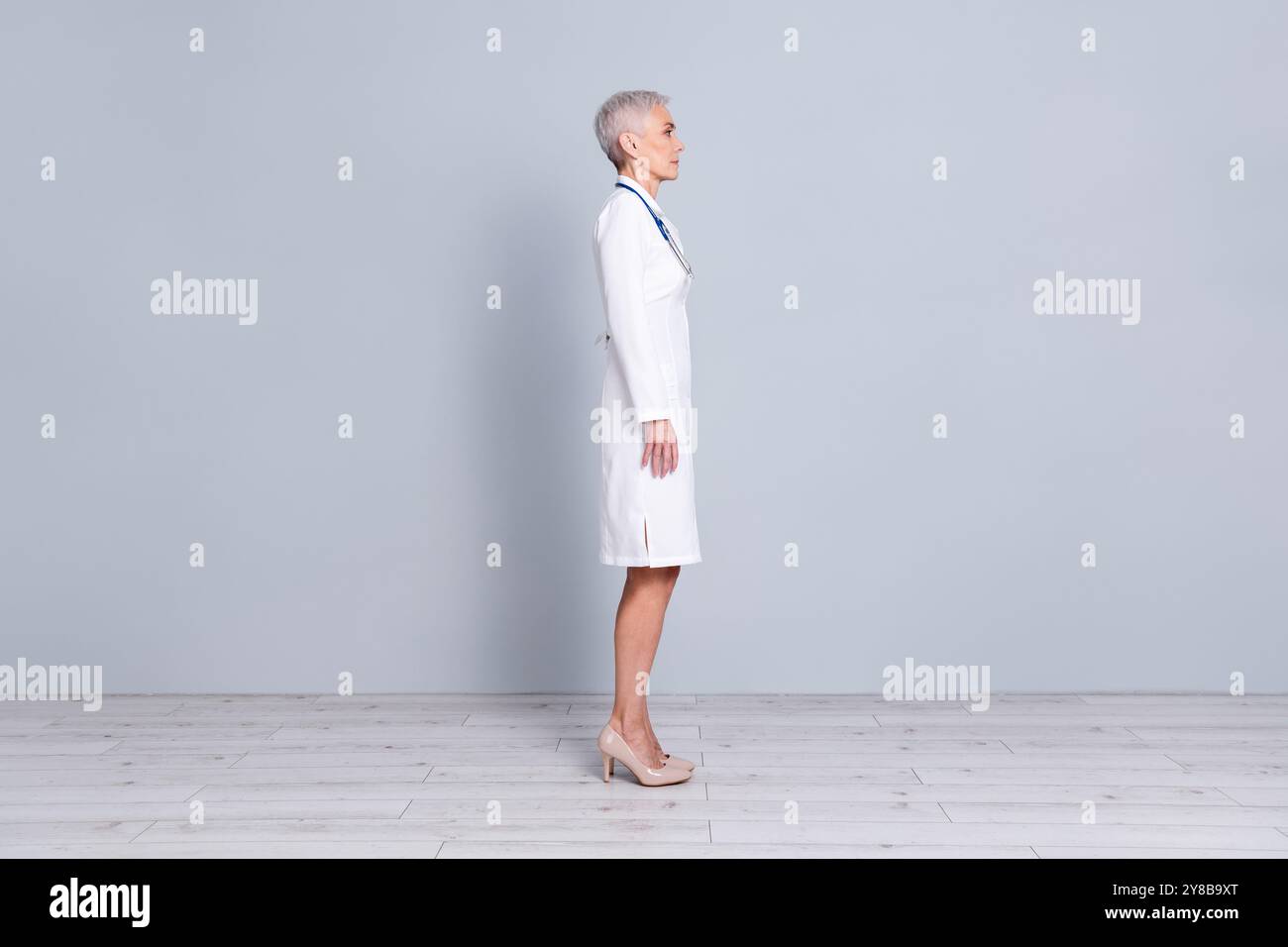 Photo pleine longueur de charmante dame senior médecin praticien qualifié porter une robe blanche isolée sur fond de couleur grise Banque D'Images