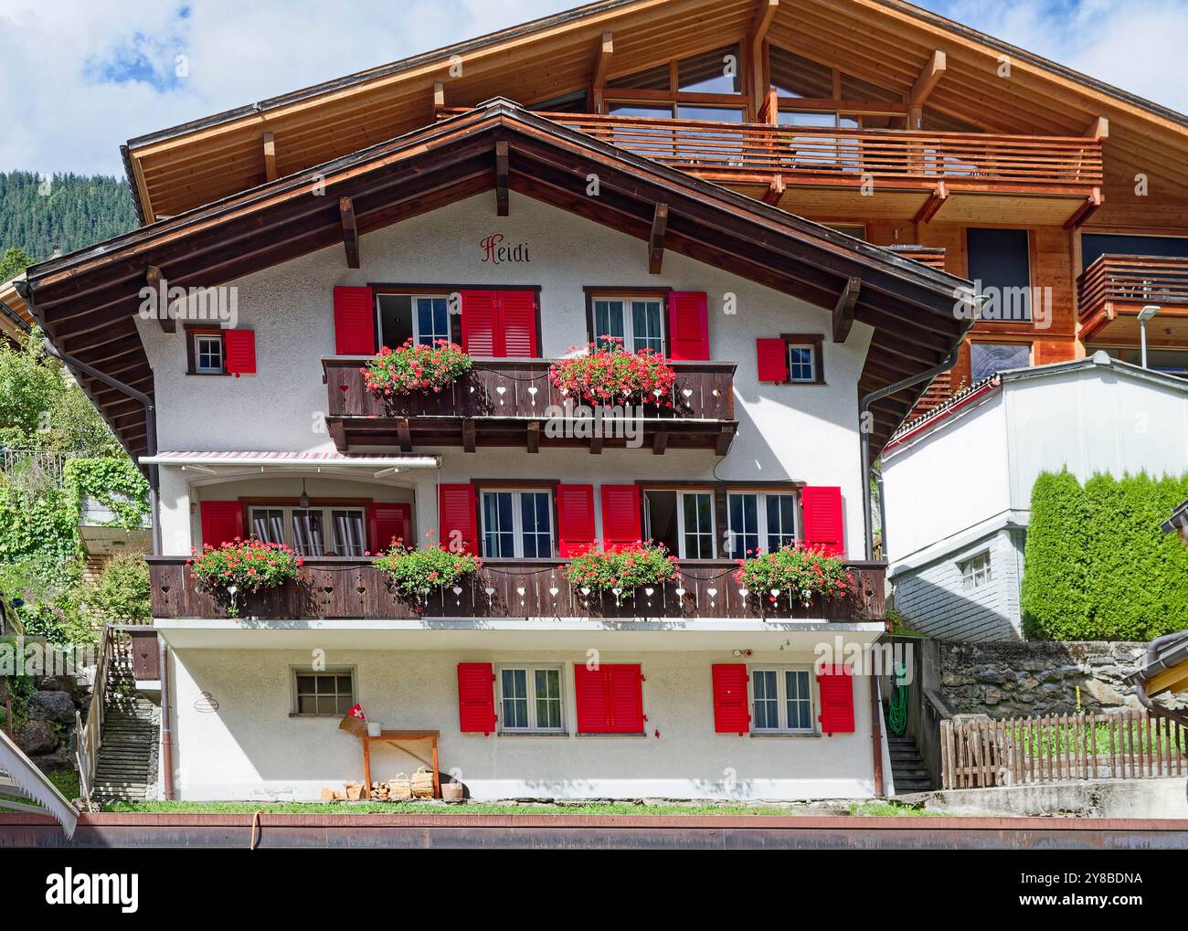 Maison suisse, style traditionnel, blanc, 2 balcons, fleurs rouges et volets, maison en bois derrière, Alpes, Europe, Grindelwald, Suisse, été Banque D'Images