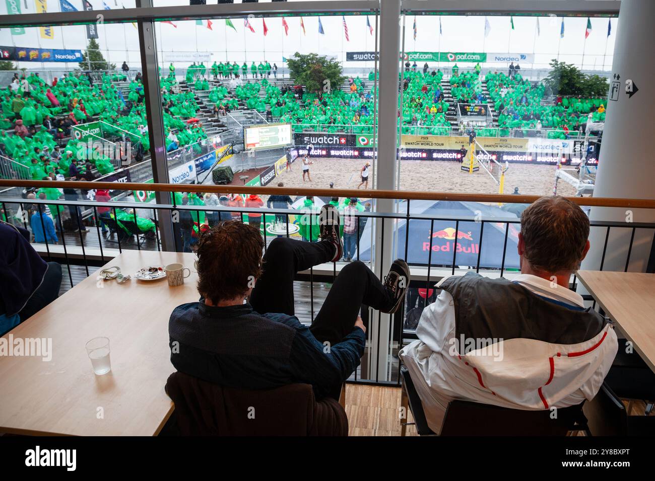 TAKING SHELTER INSIDE, SUMMER STORM, BEACH VOLLEY, MARIEHAMN, 2011 : certains fans se réfugient dans le café du théâtre alors que la foule se couvre avec des ponchos jetables alors qu'une énorme tempête estivale balaye le stade avec un déluge de pluie pendant les demi-finales en août 2011 au PAF Open à Mariehamn, Åland, Finlande. Photographie : Rob Watkins. INFO : entre 2009-2013, le tournoi PAF Open Beach Volleyball était un événement annuel organisé à Mariehamn, Åland, Finlande. Il a attiré les meilleures équipes et joueurs internationaux en tant que partie du classement du circuit mondial officiel de la FIVB, mettant en vedette le b de haut niveau Banque D'Images