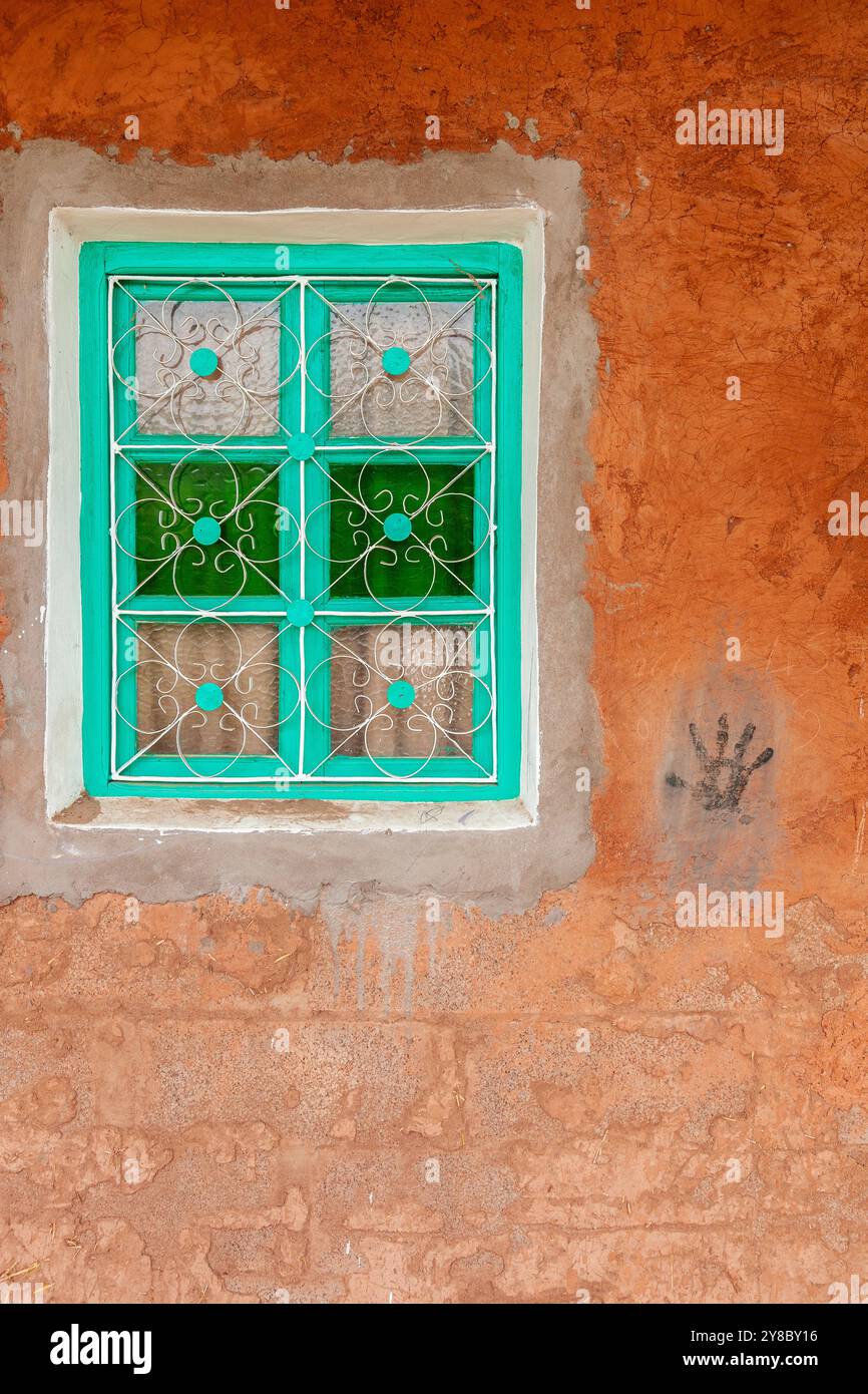 Fenêtre avec cadre vert contre un mur rouge-ocre, sur lequel apparaît l'empreinte noire d'une main Banque D'Images