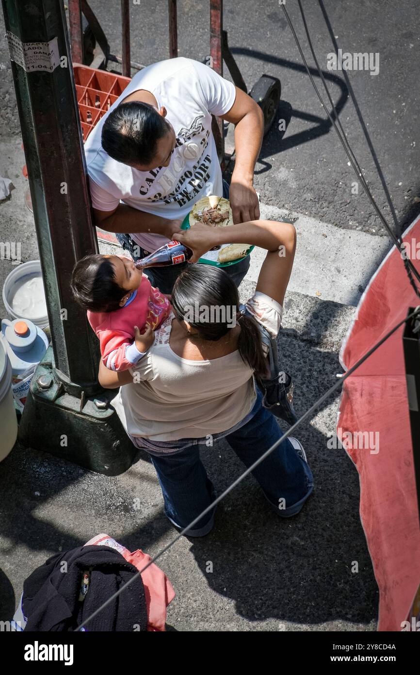 Mexico City CDMX 2009 : pauvre déjeuner en famille mexicaine ; mère donne à son enfant une boisson Coca-Cola et mari mange des tacos, au coin de la ville Banque D'Images