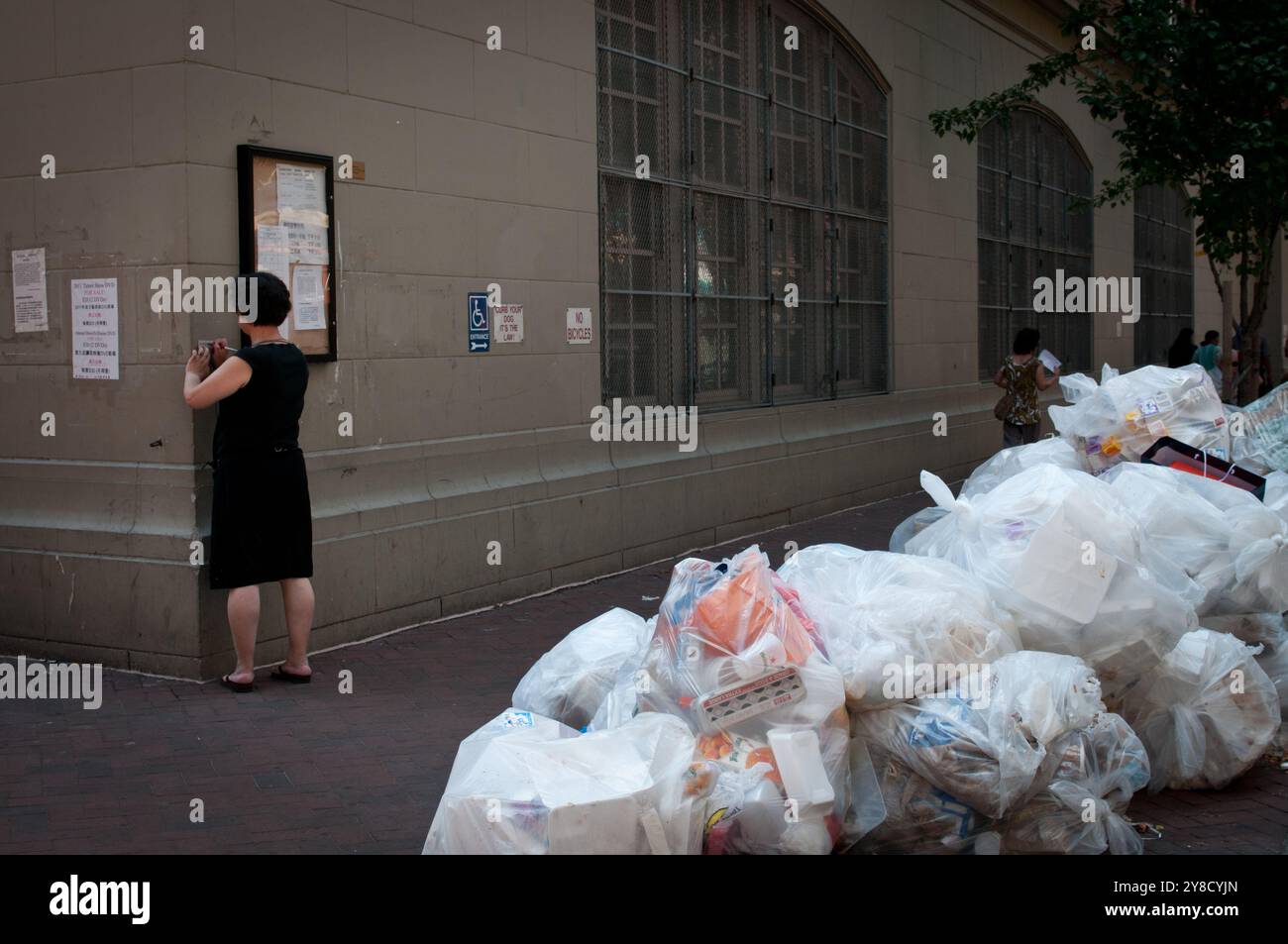 New York, États-Unis, 11 juillet 2011 : une femme est debout sur le trottoir en train de lire une annonce sur un mur, avec une grande pile de sacs poubelle au premier plan. Banque D'Images