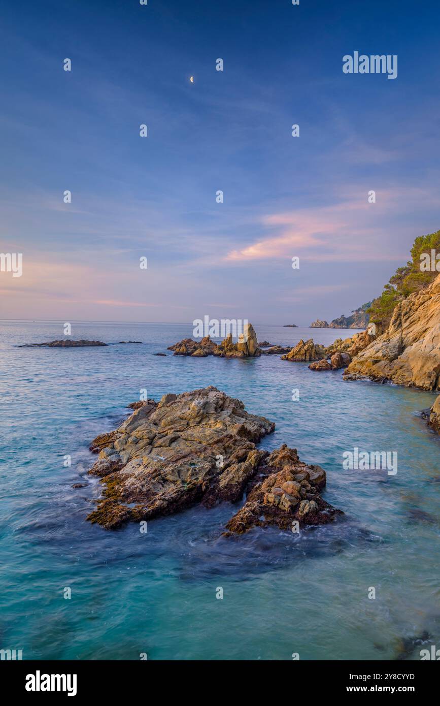 Lever de soleil rouge à Cala sa Boadella et avec la lune décroissante, à Lloret de Mar, Costa Brava (la Selva, Gérone, Catalogne, Espagne) Banque D'Images