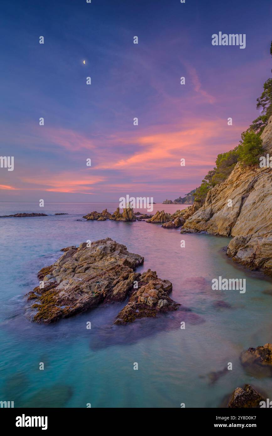 Lever de soleil rouge à Cala sa Boadella et avec la lune décroissante, à Lloret de Mar, Costa Brava (la Selva, Gérone, Catalogne, Espagne) Banque D'Images