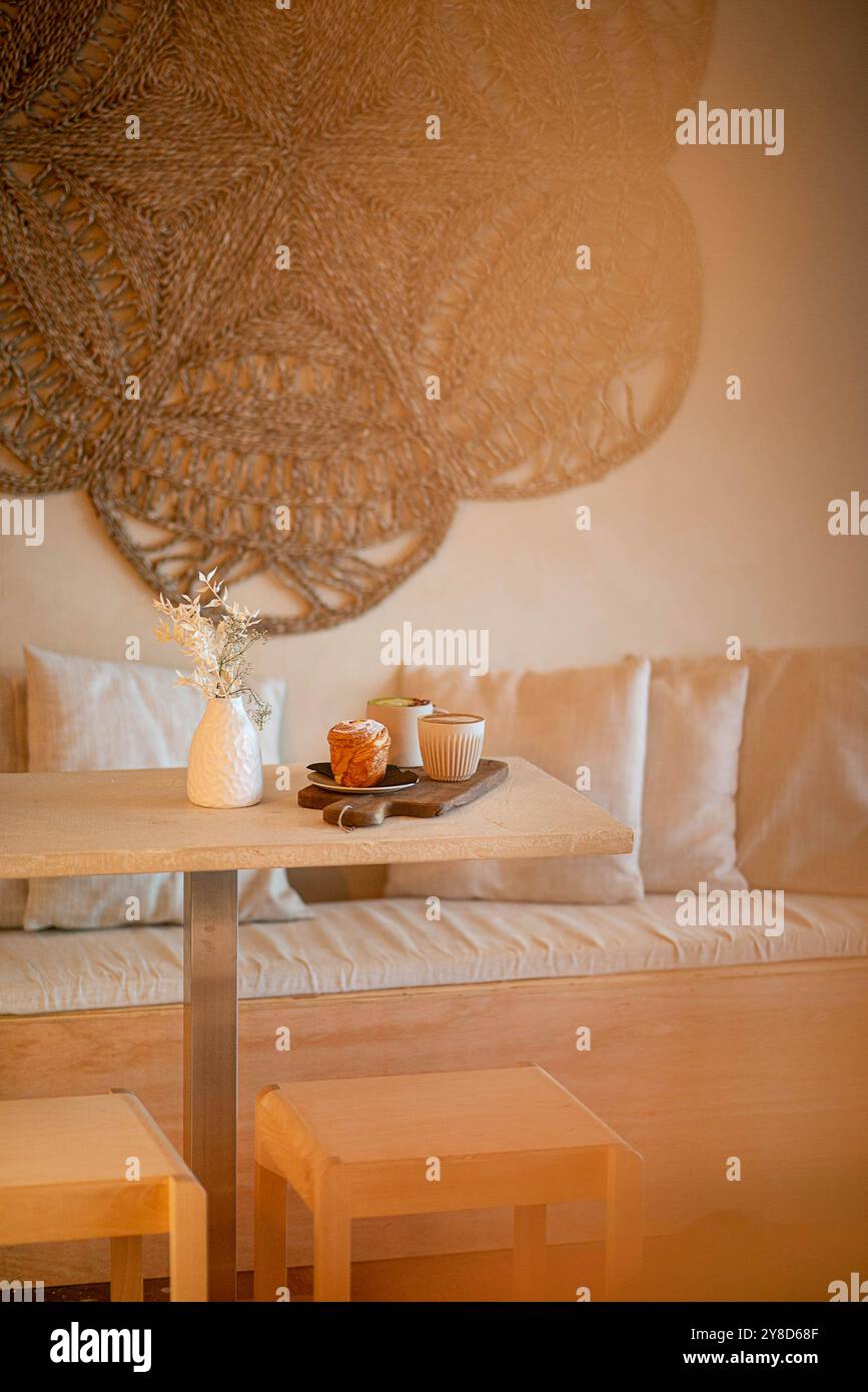 Table de café confortable avec deux tasses à café en céramique, une pâtisserie, un vase blanc avec des fleurs séchées et un magazine, baigné de lumière naturelle chaude. Banque D'Images