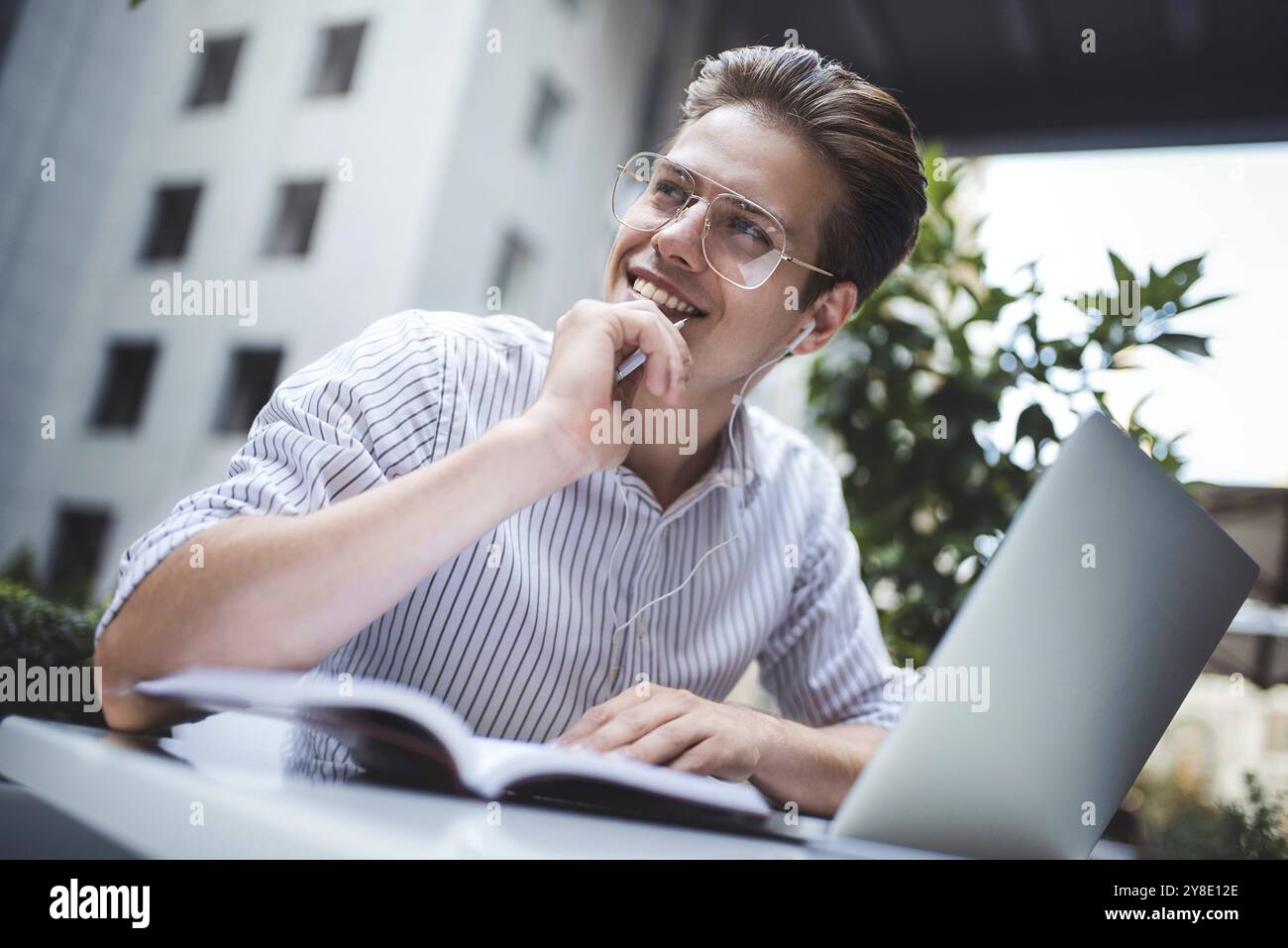 Heureux homme d'affaires beau mélange sa pause et son travail à l'extérieur, homme d'affaires avec des écouteurs écrire quelques nouvelles idées dans le cahier assis dans le café Banque D'Images