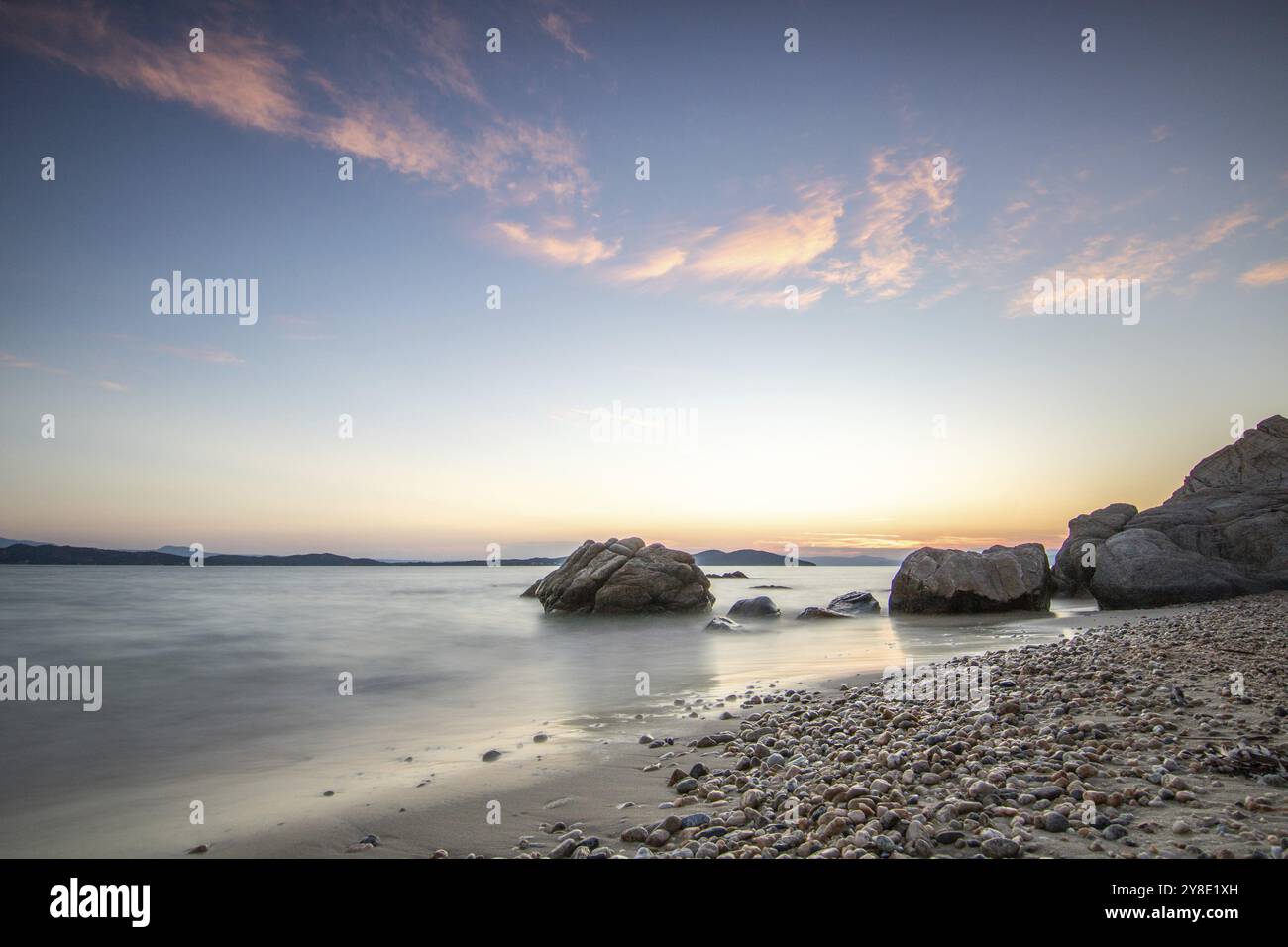 Vue à travers les rochers sur une plage de sable dans le coucher du soleil. Paysage tourné avec vue à l'horizon sur la large mer à la côte d'Ouranoupoli, Thessaloni Banque D'Images