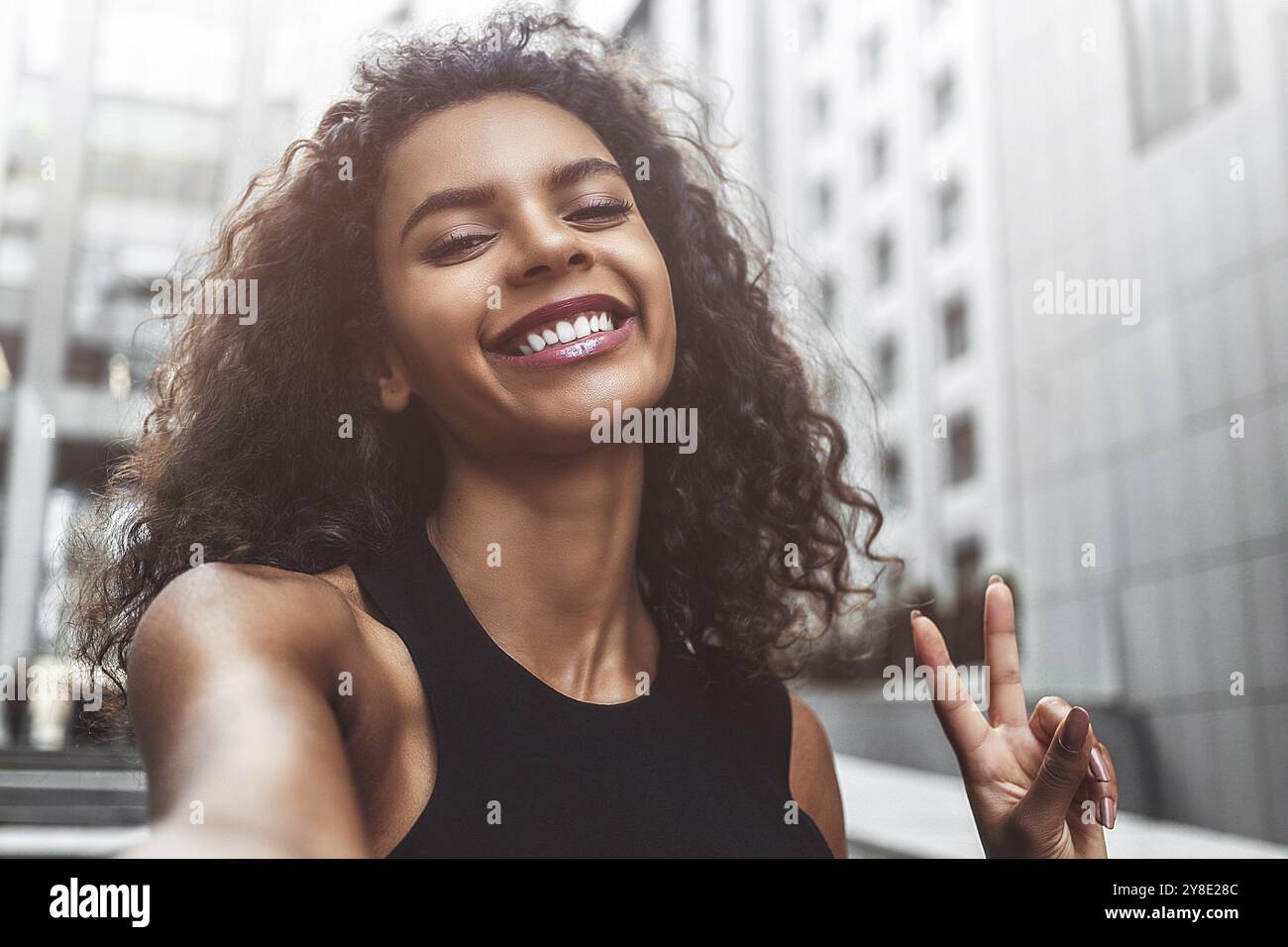 Portrait en plein air belle femme afroamerican heureuse prenant selfie photo souriant rire avec des dents parfaites dans la rue Banque D'Images