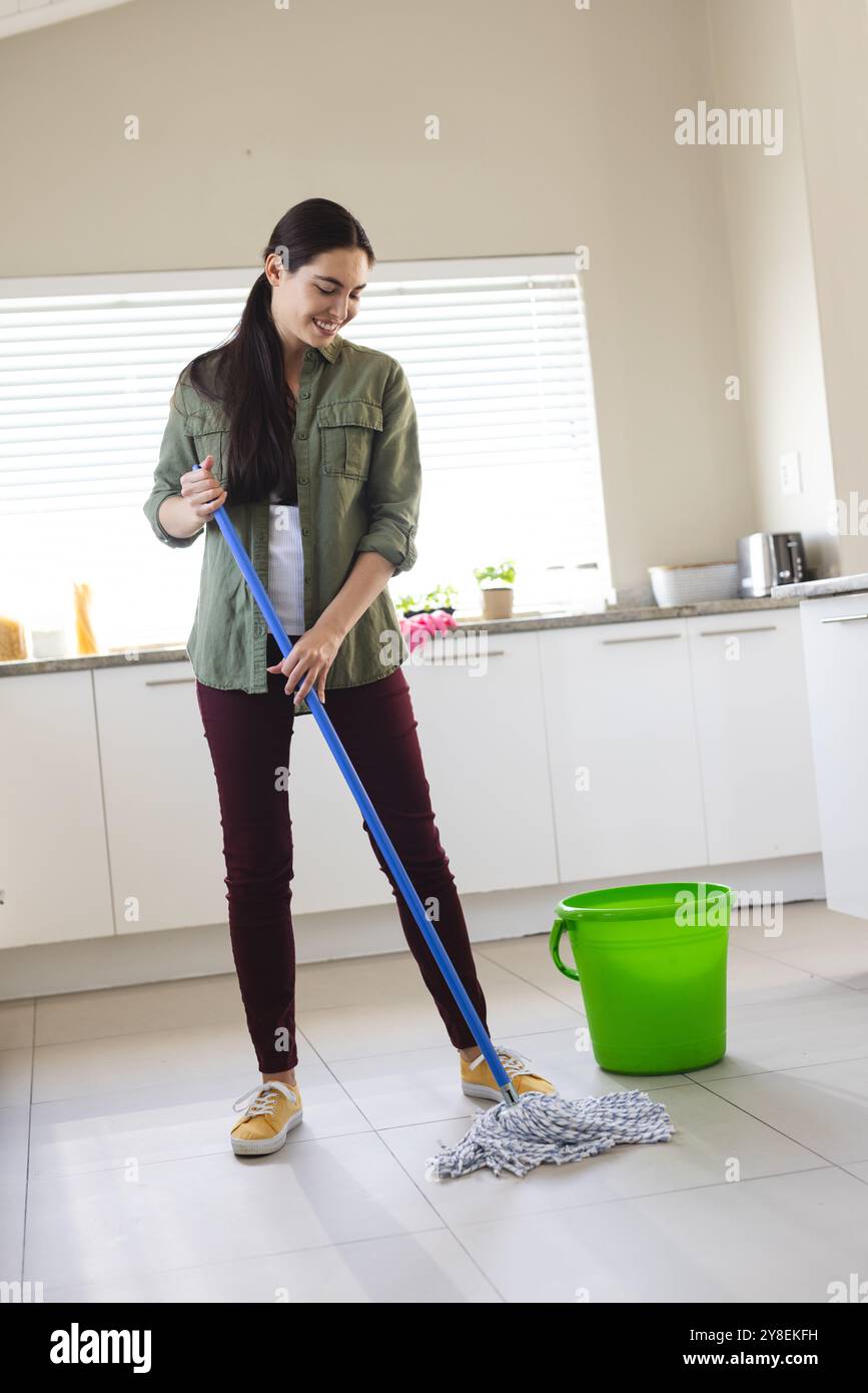 Pleine longueur de jeune femme caucasienne souriante nettoyant le sol avec vadrouille humide à la maison, espace de copie Banque D'Images