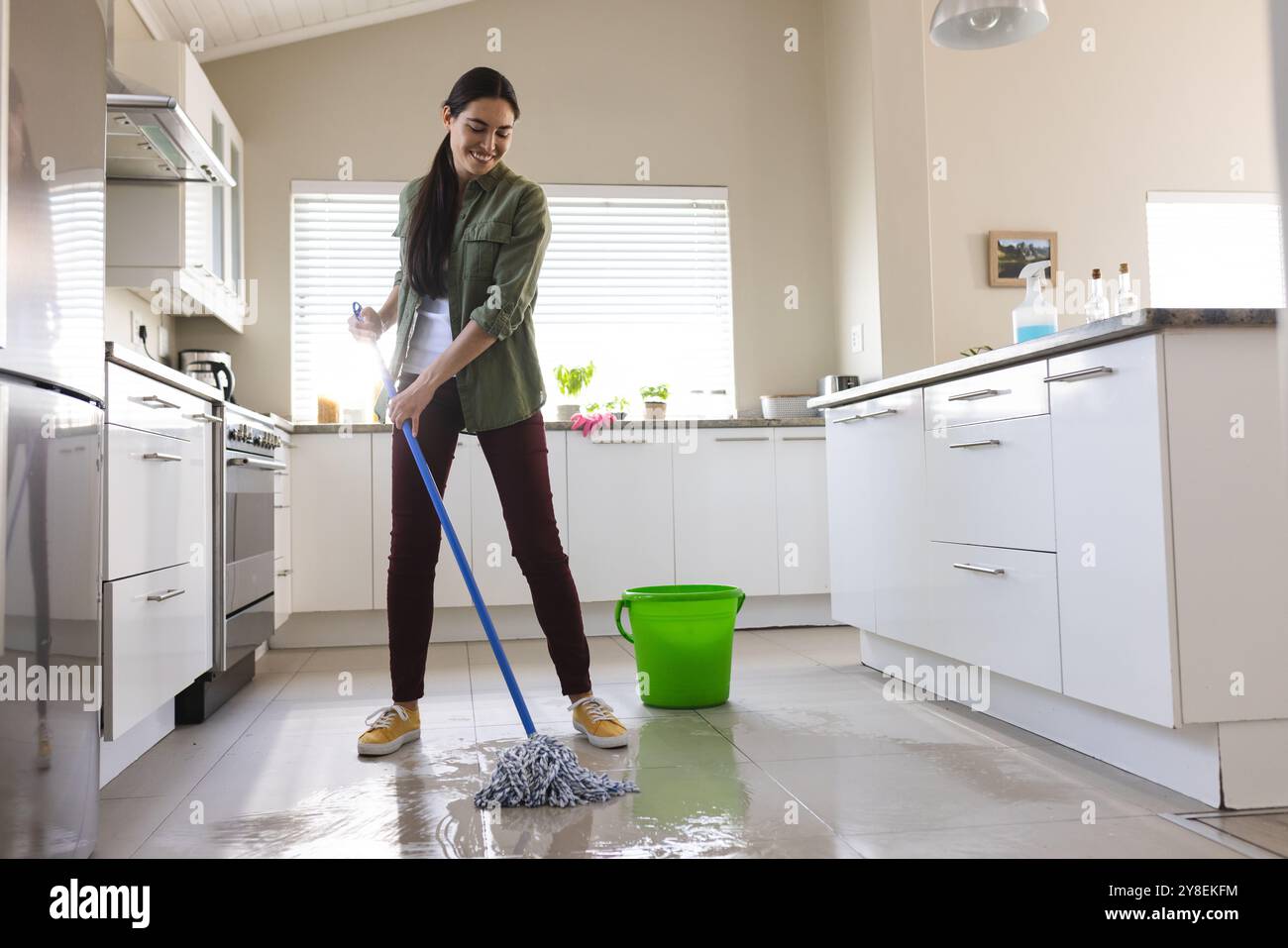 Jeune femme souriante caucasienne nettoyant le sol de la cuisine avec vadrouille humide à la maison, espace de copie Banque D'Images