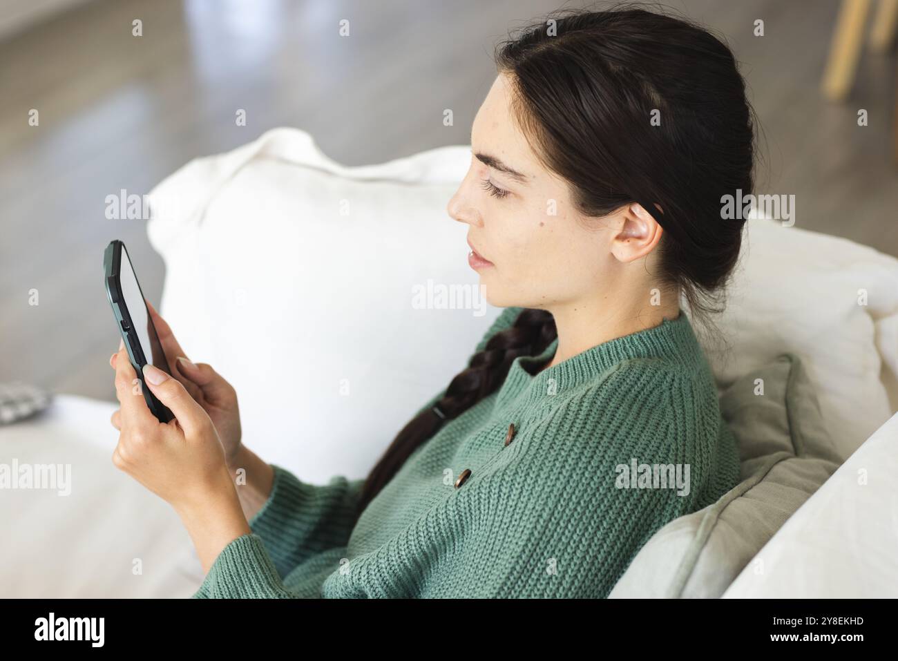 Vue latérale de la jeune femme caucasienne discutant sur téléphone intelligent tout en se relaxant sur le canapé à la maison Banque D'Images