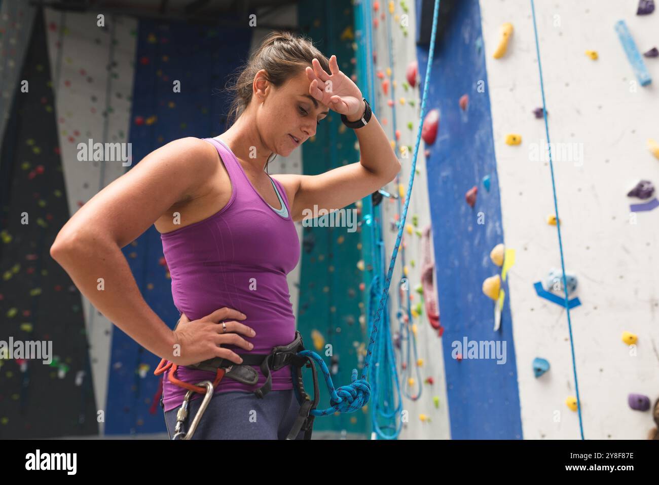 Femme caucasienne prenant repos frottant son front contre le mur d'escalade intérieur Banque D'Images