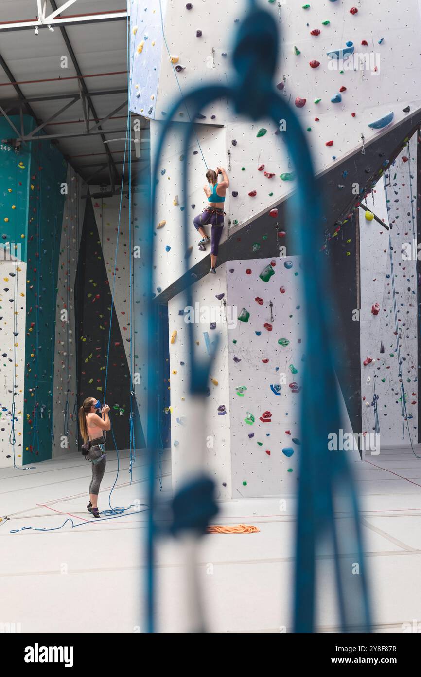 Deux femmes caucasiennes portant des masques faciaux en utilisant des cordes pour grimper au mur à la salle d'escalade intérieure Banque D'Images