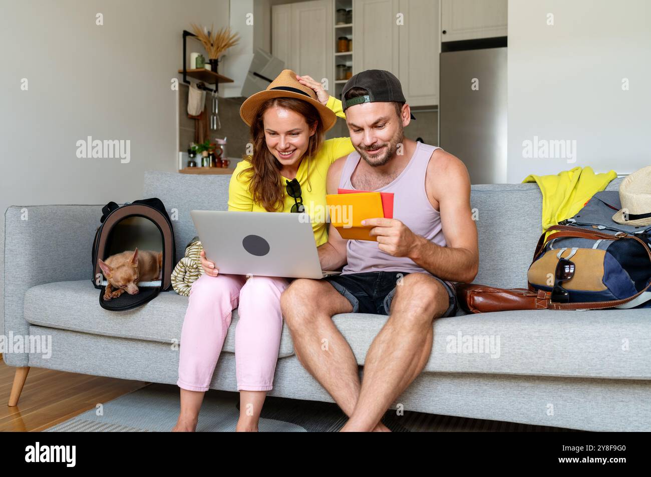 Couple avec petit chien dans le transporteur à la maison finalisant les plans de voyage avant le départ, en vérifiant les données de réservation. Banque D'Images