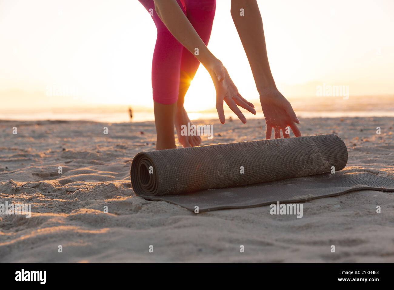 Milieu de la section de femme caucasienne roulant tapis de yoga à la plage Banque D'Images