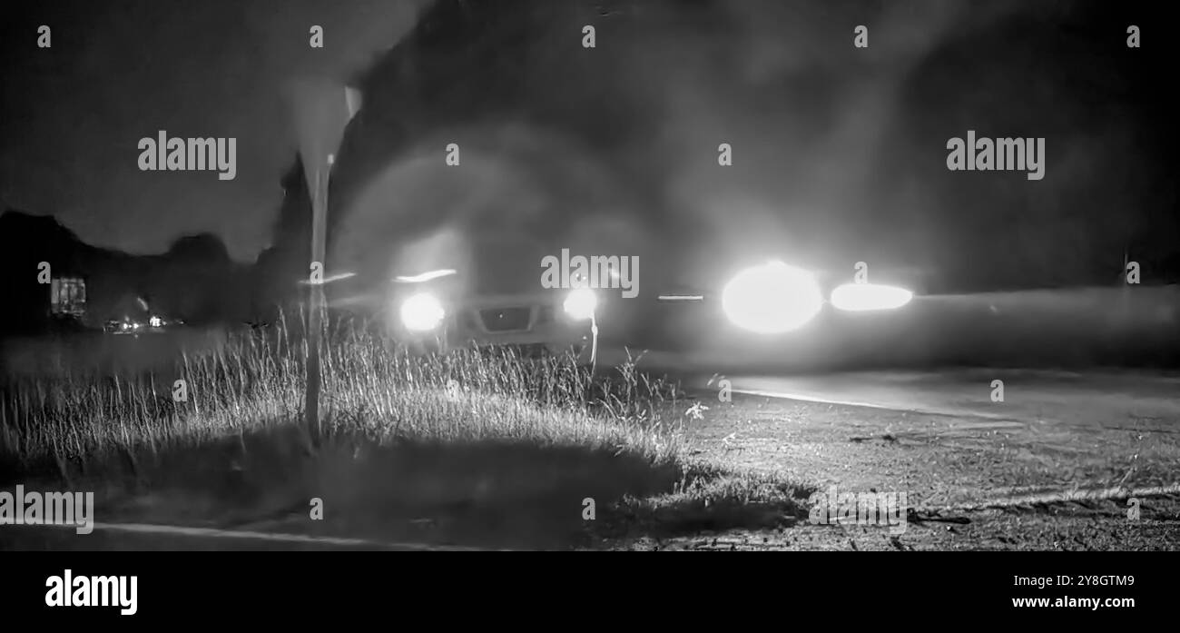 Voiture conduisant la nuit, avec leurs phares allumés et en mouvement (noir et blanc) Banque D'Images