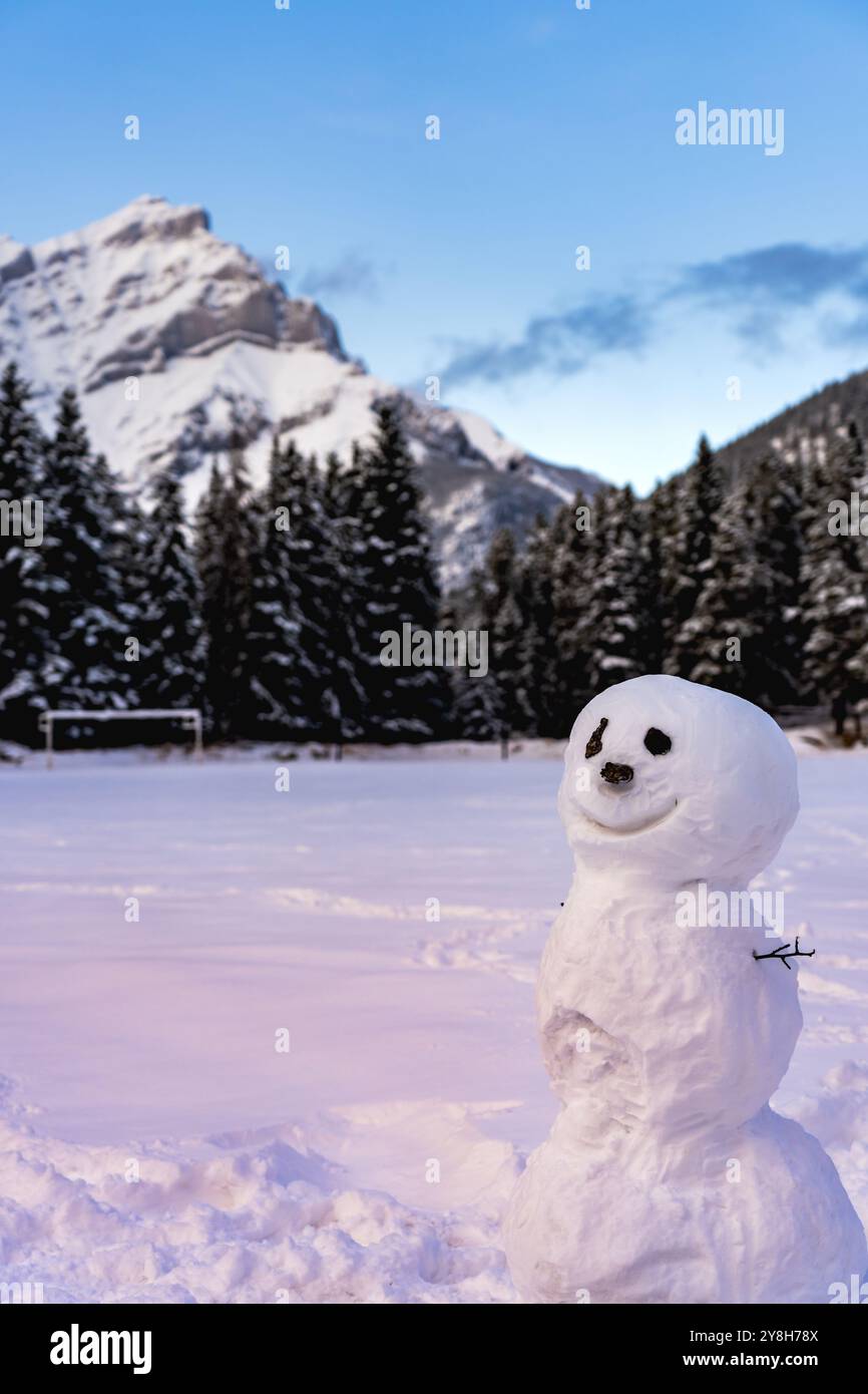 Un bonhomme de neige souriant dans l'aire de jeux enneigée. Cascade Mountain et arbres en arrière-plan. Parc national Banff, Rocheuses canadiennes. Banque D'Images